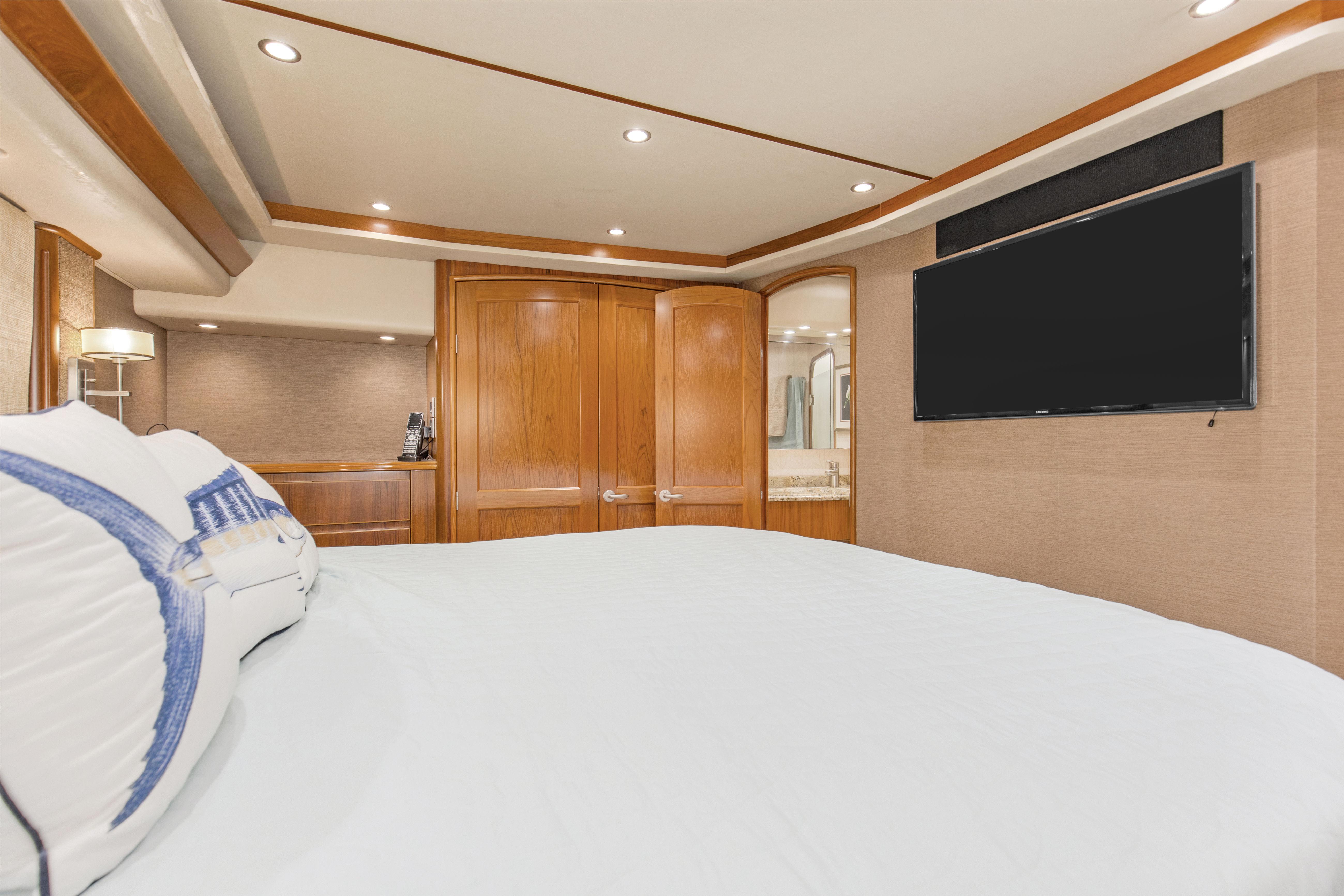 Luxurious bedroom interior of 2015 Viking 70 Convertible yacht with TV and wooden accents.