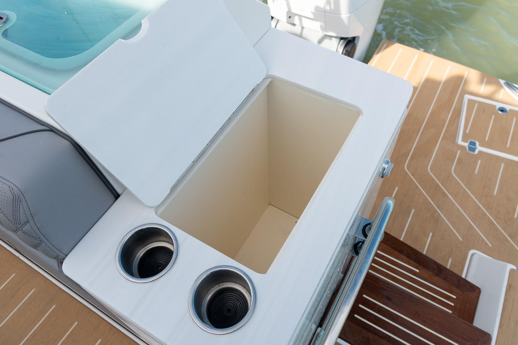 Open storage compartment on 2026 Regal LX43 boat with cup holders and wooden deck.