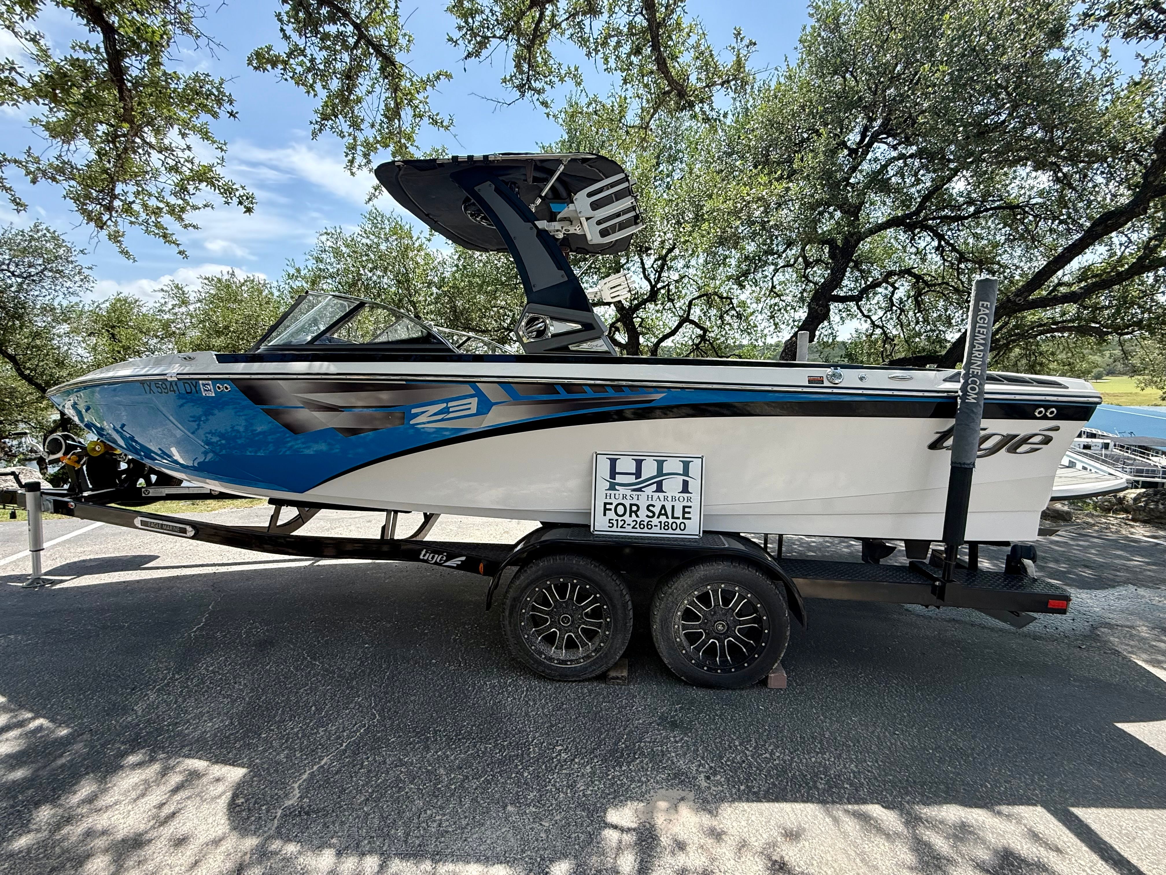 A blue and white 2017 Tigé Z3 boat on a trailer under trees.