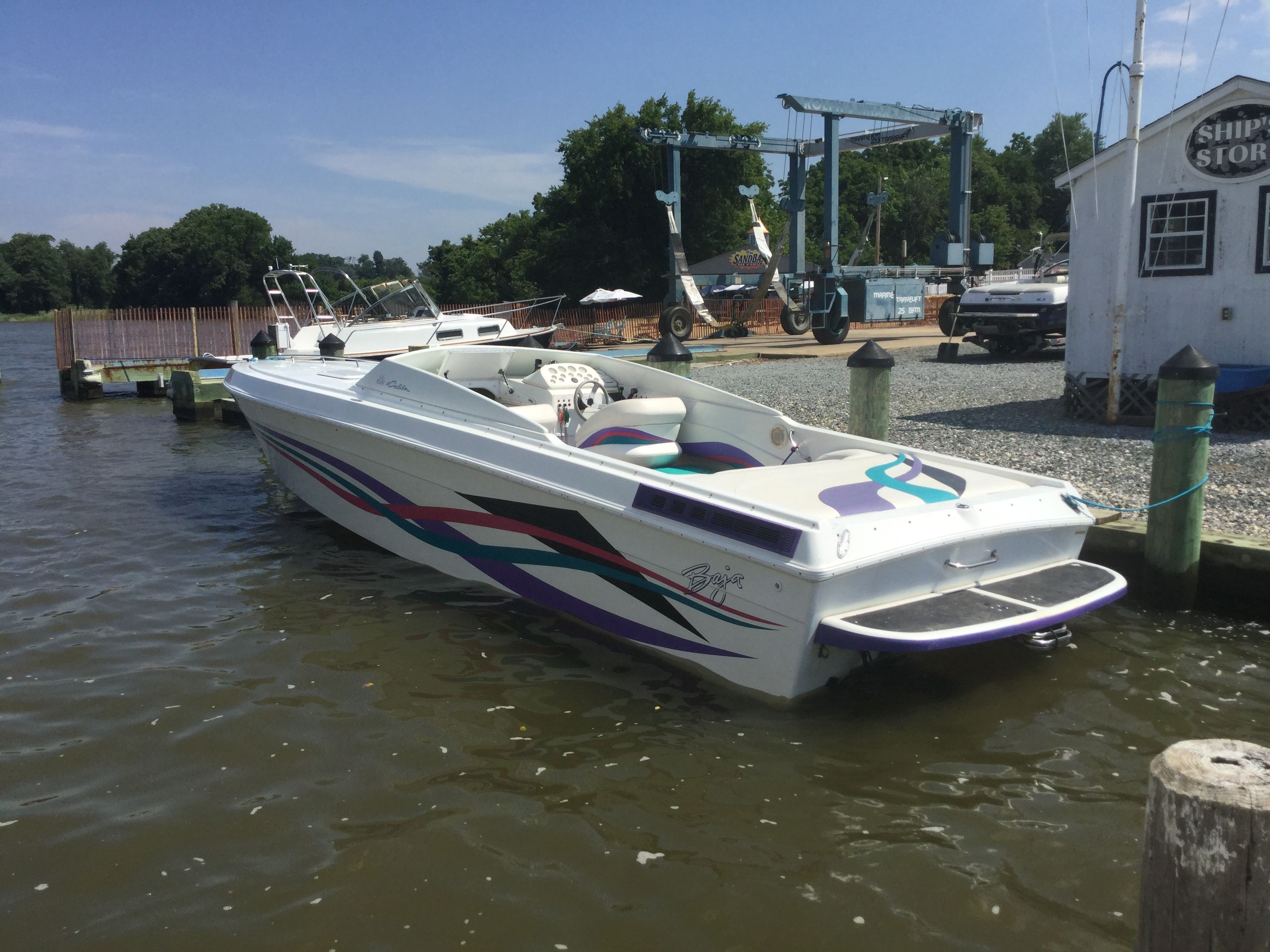 A 1995 Baja Caliber boat docked. It features colorful stripes and an open cockpit.