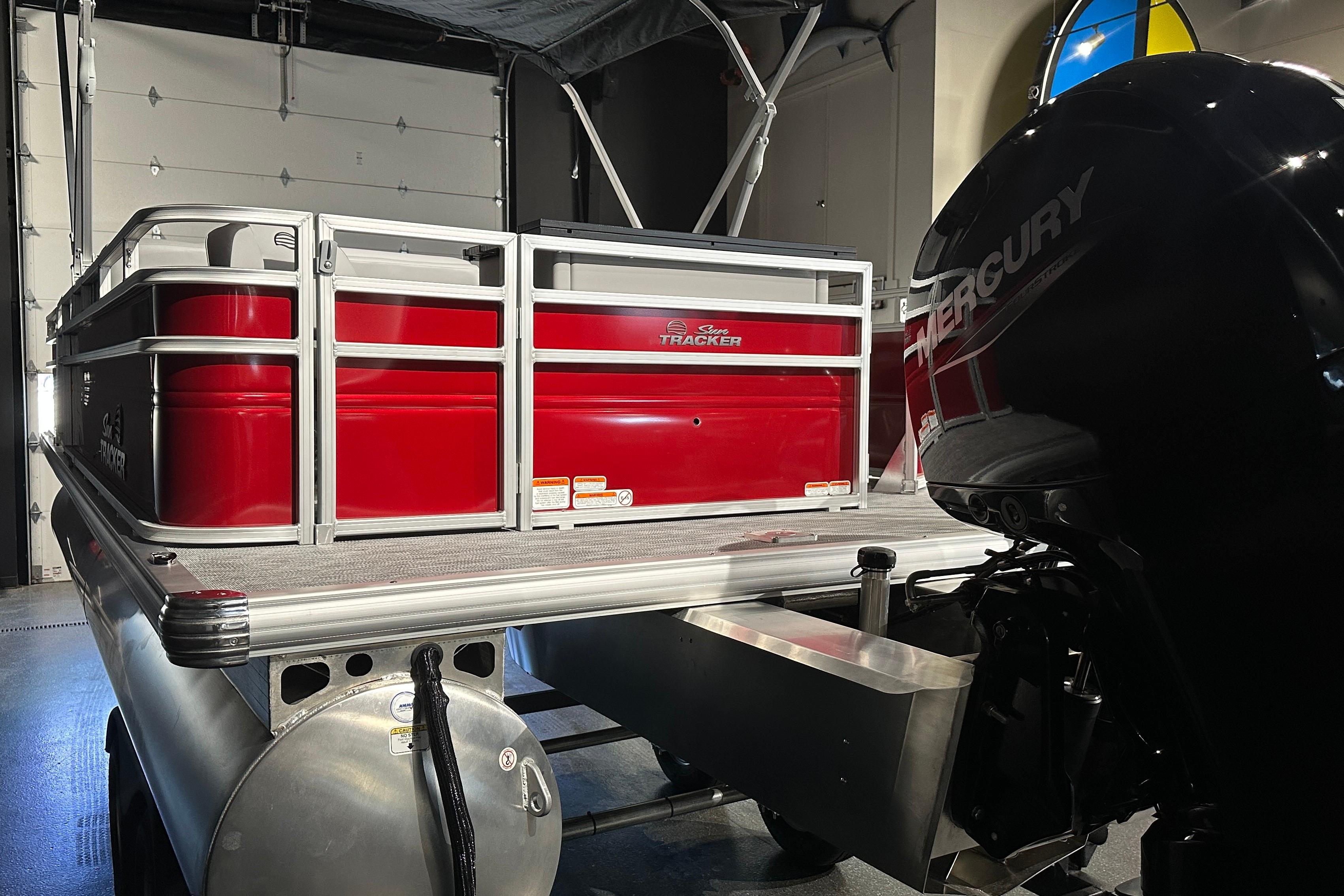 2026 Sun Tracker SportFish 22 DLX pontoon boat with Mercury engine in a garage.