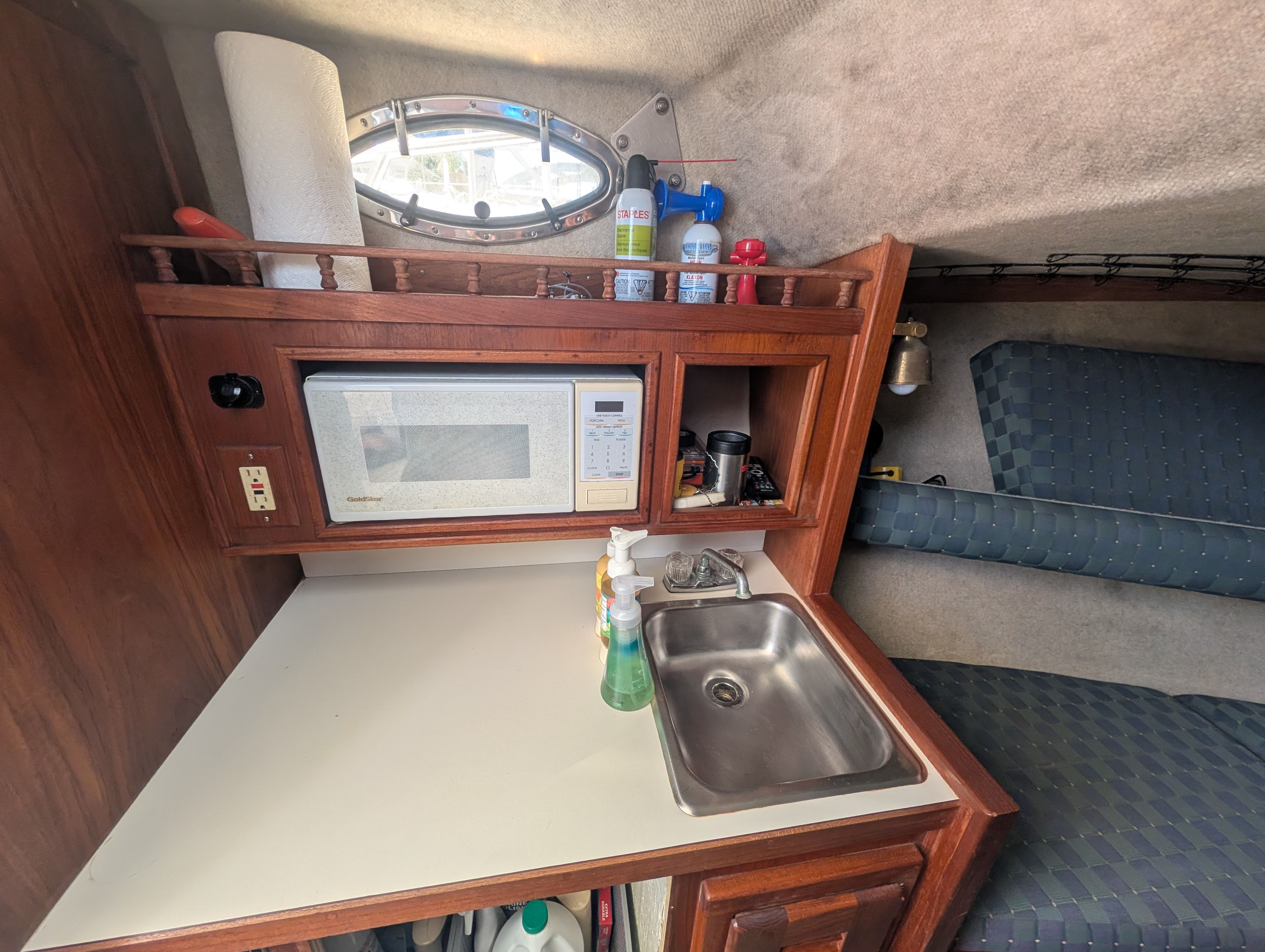 Small kitchenette in a boat with microwave, sink, and storage.