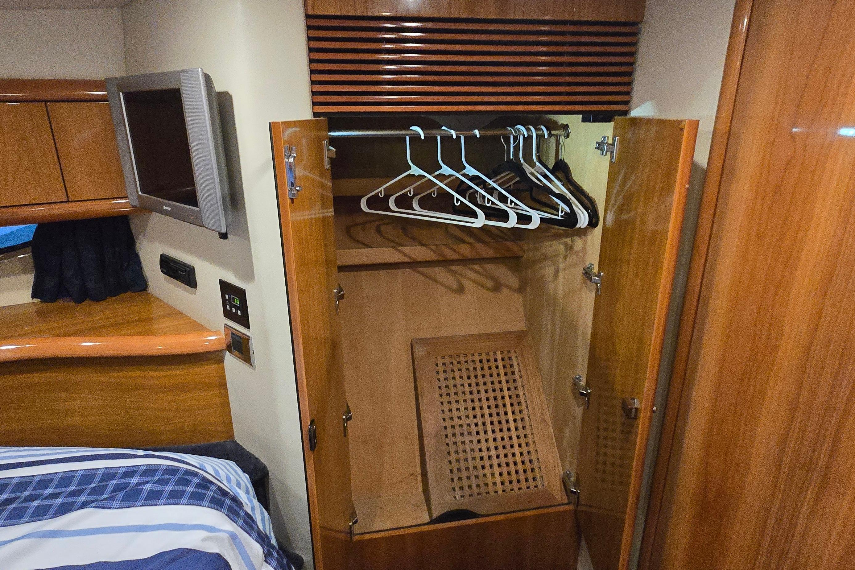 Interior of 2004 Sunseeker Camargue 50 yacht with open wooden wardrobe and hangers.
