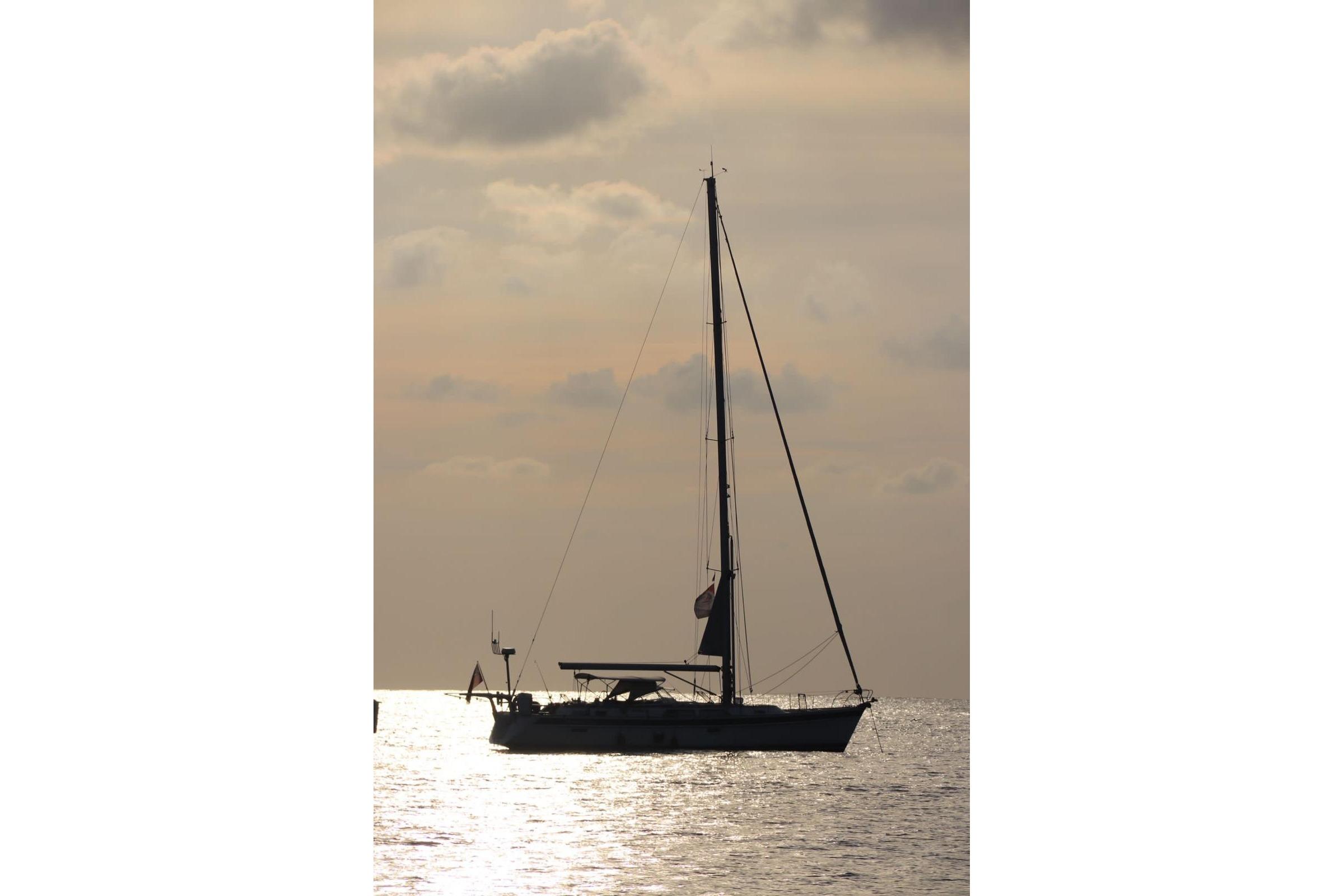 Silhouette of a 2020 Hallberg-Rassy 48 MkII sailboat on calm waters at sunset.