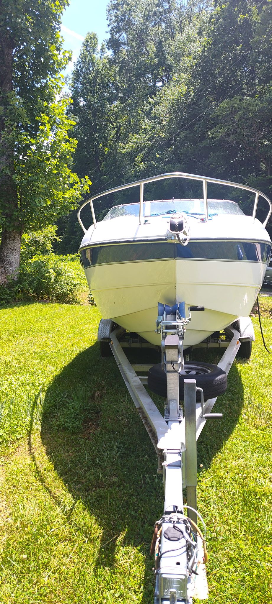 A 2002 Stingray 240 CR boat on a trailer, surrounded by trees and grass.