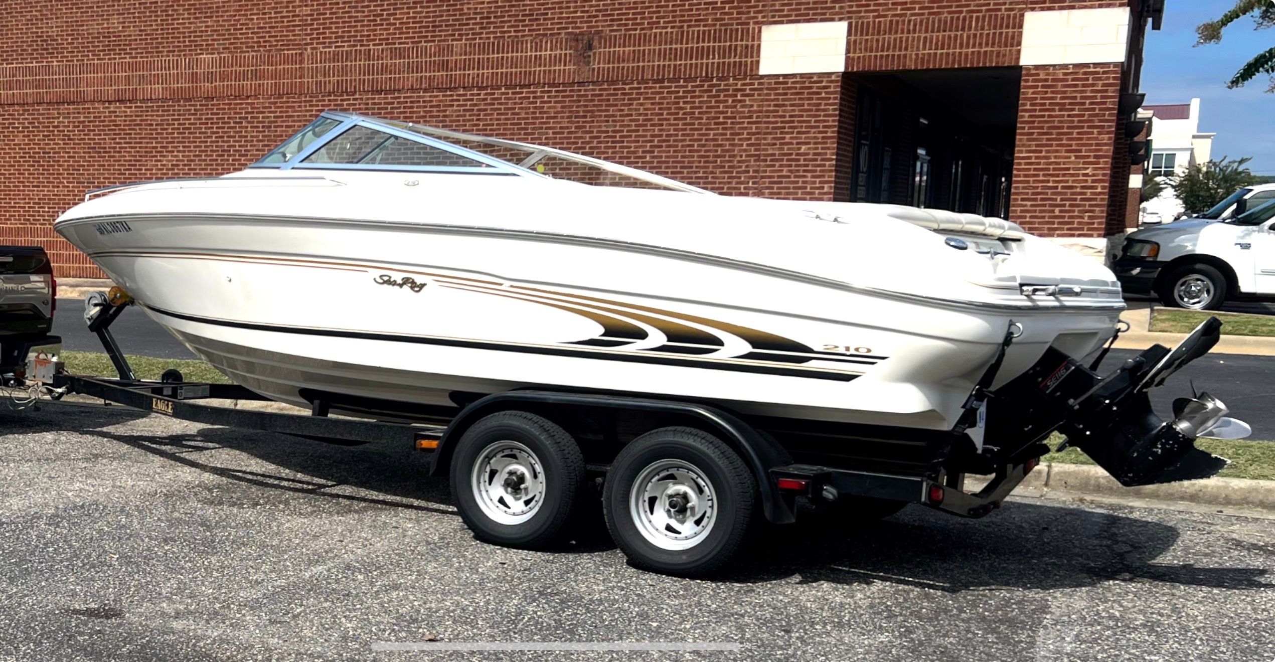 A white 1999 Sea Ray 210 Bow Rider Signature boat on a trailer in front of a brick building.