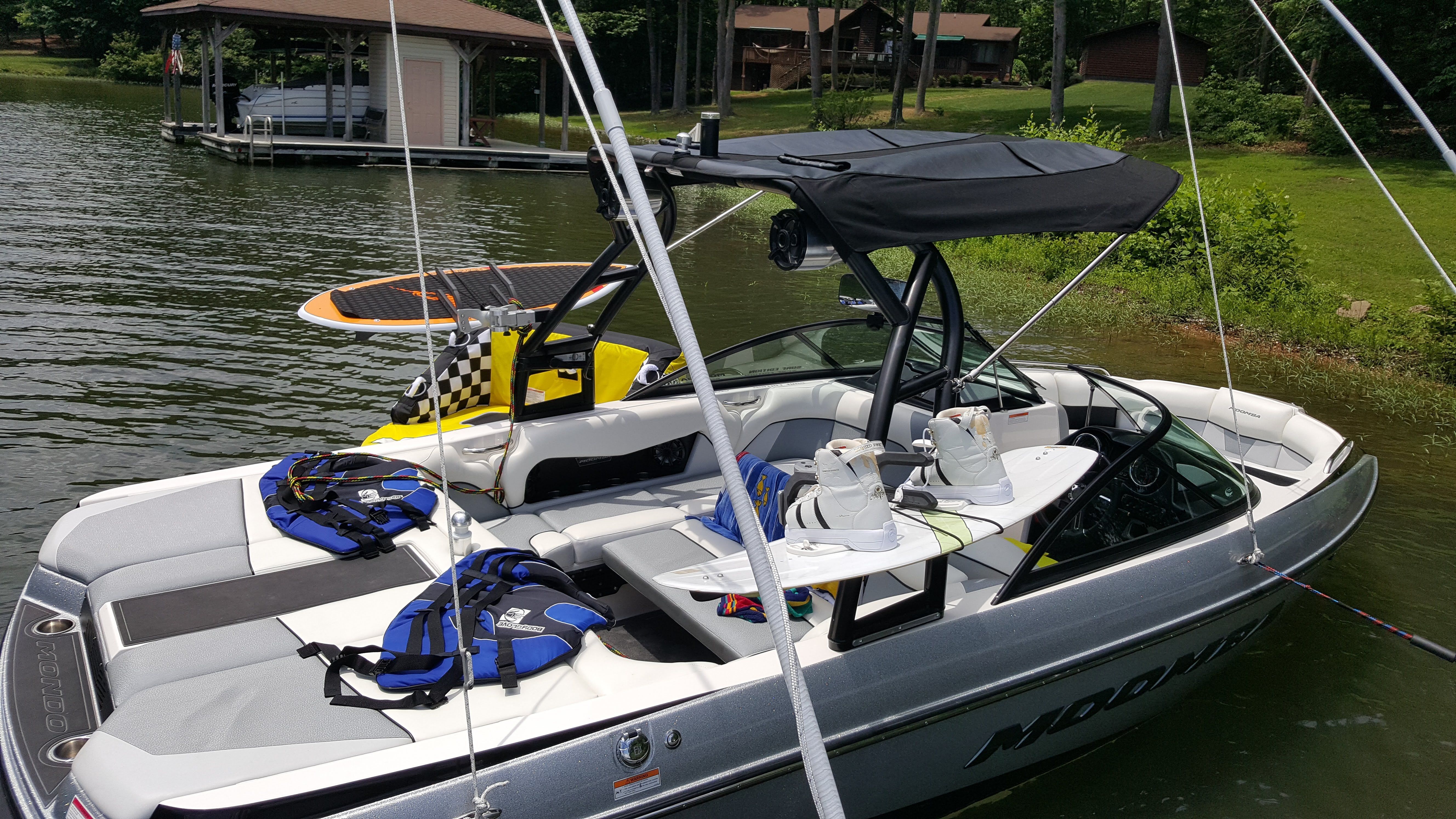 A 2016 Moomba Mondo boat is docked by the lakeside. It is equipped with watersport gear.