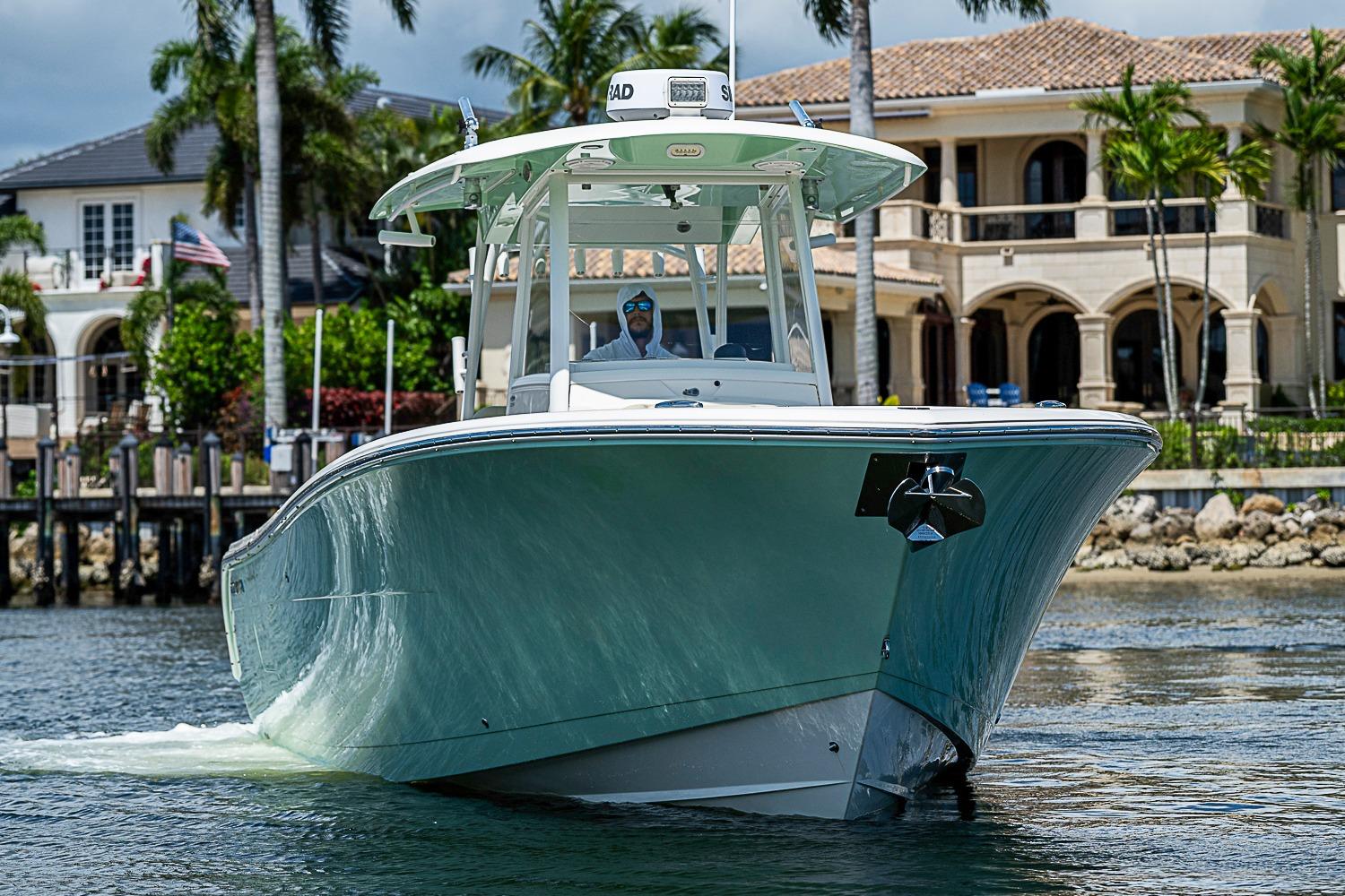 2019 Cobia 320 Center Console boat cruising near luxury waterfront homes.