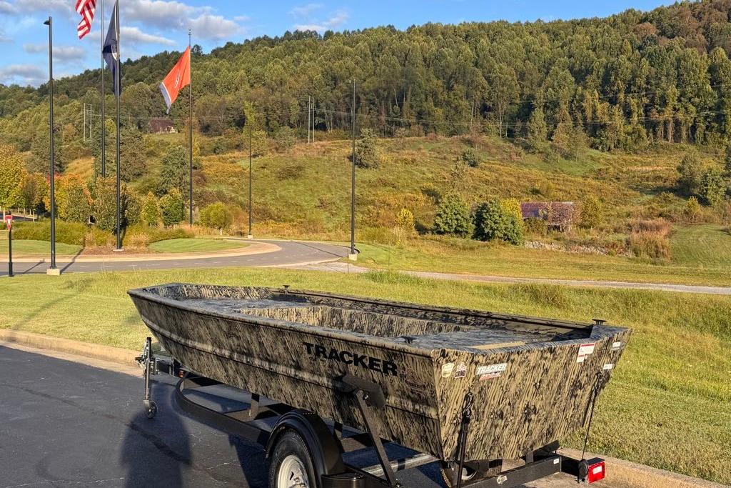 2026 Tracker Grizzly 1754 Utility boat on trailer, scenic background with flags and hills.