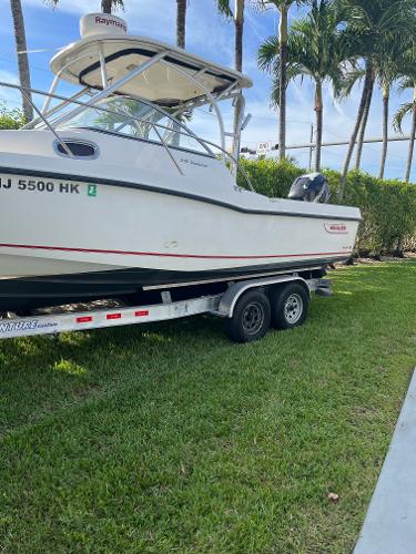 2011 Boston Whaler 235 Conquest boat on trailer, parked on grass with palm trees.