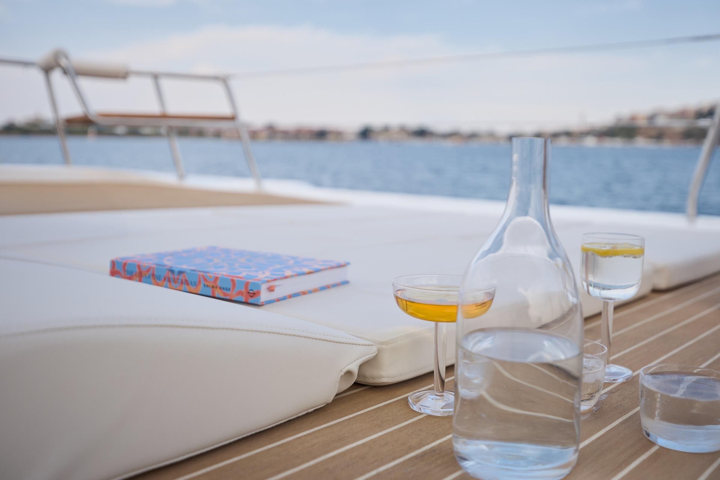 Luxurious deck of 2025 Omaya 50 Power Catamaran with drinks and book, overlooking serene waters.