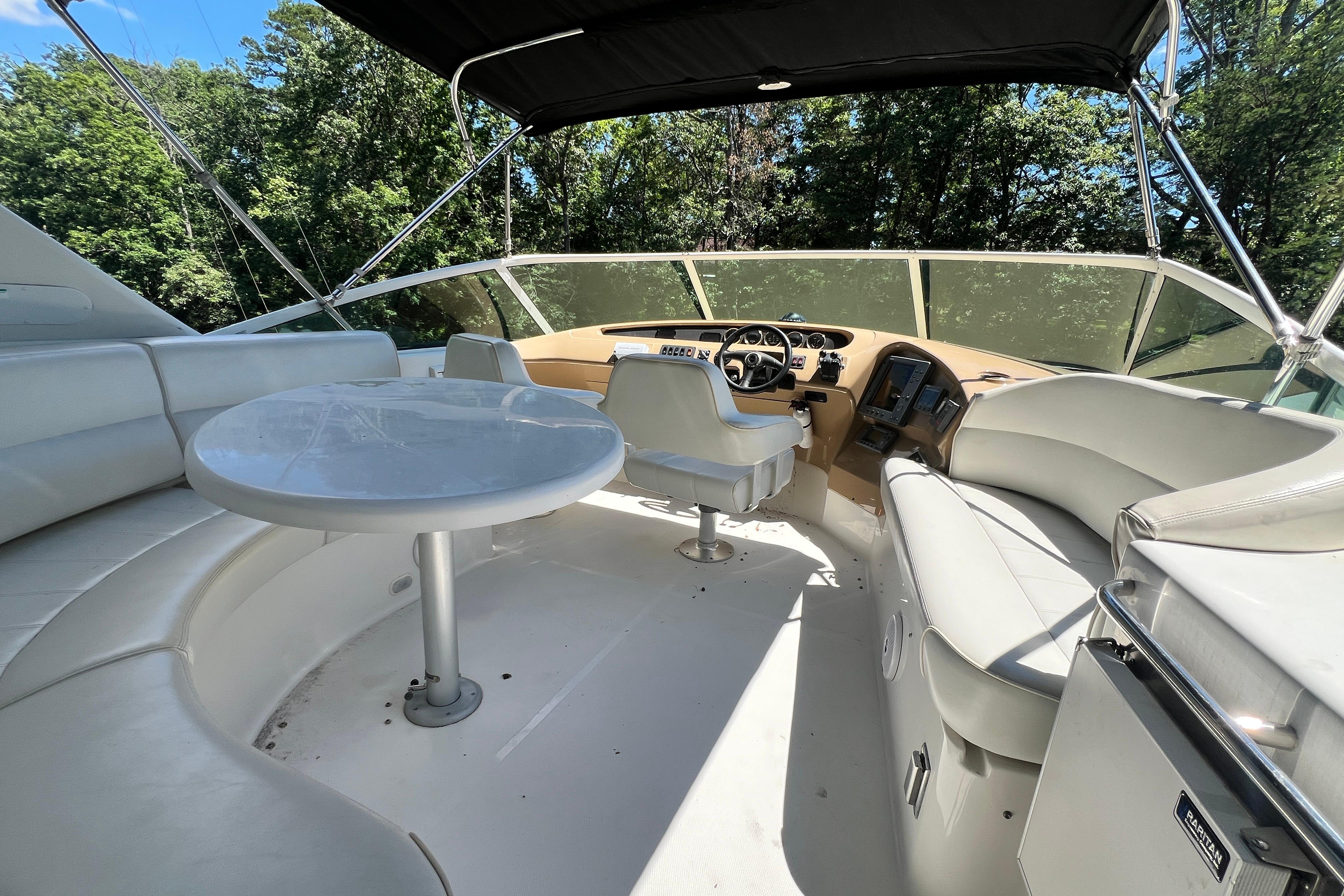 2003 Carver 450 Voyager Pilothouse interior with seating and helm, surrounded by lush greenery.