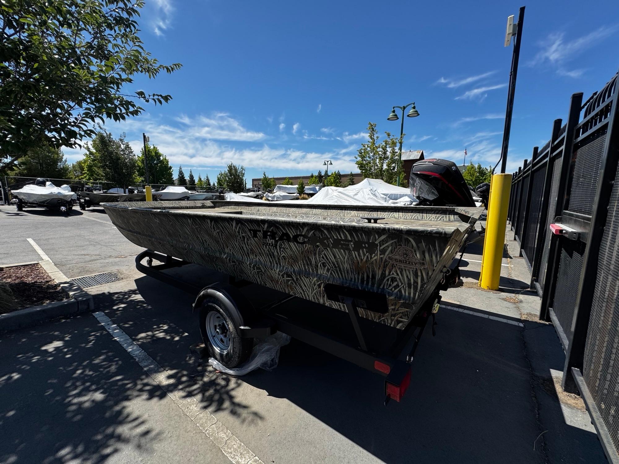 2025 Tracker GRIZZLY 2072 Utility boat on trailer in parking lot, sunny day.