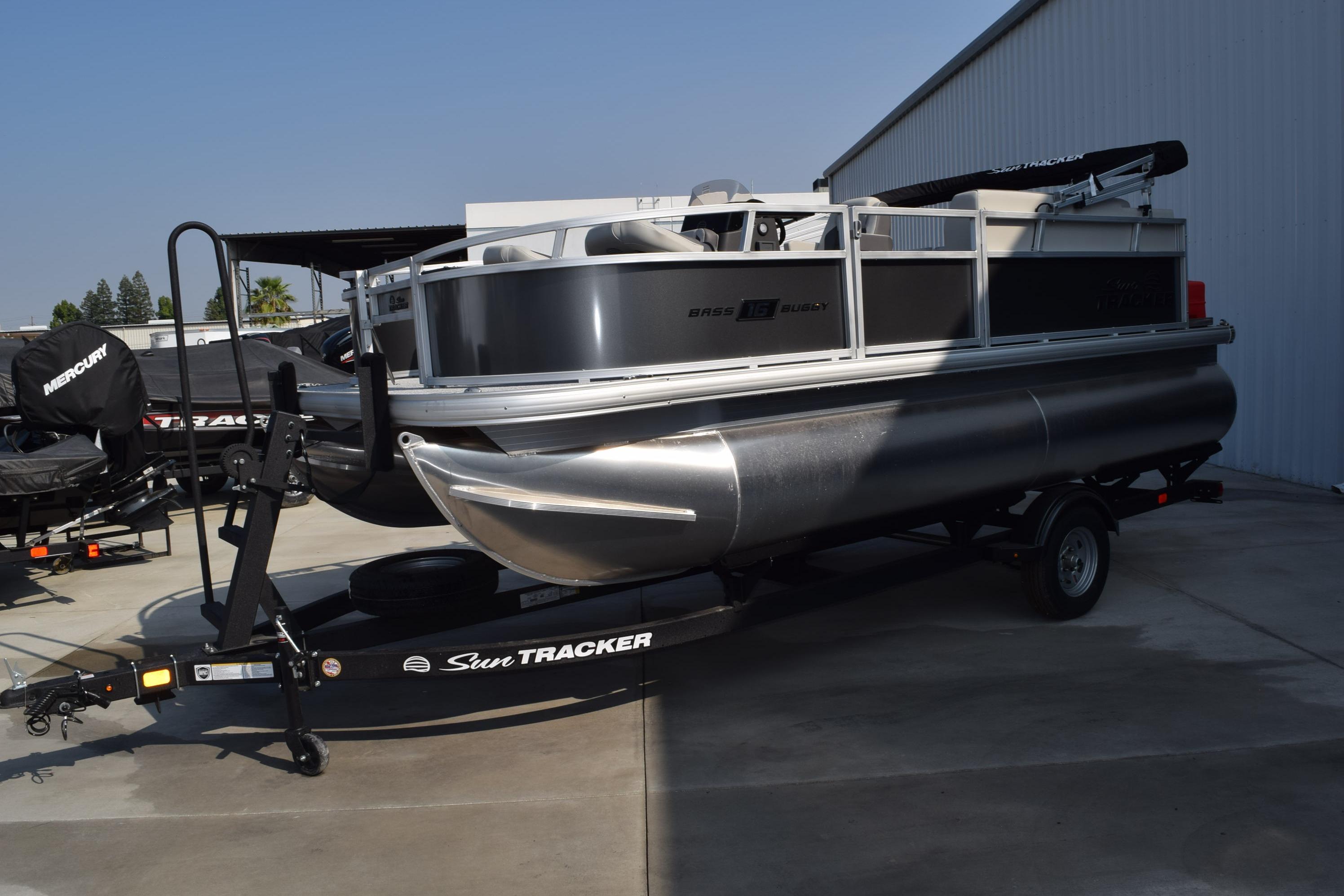 2026 Sun Tracker Bass Buggy 16 XL Select pontoon boat on trailer, parked outdoors.