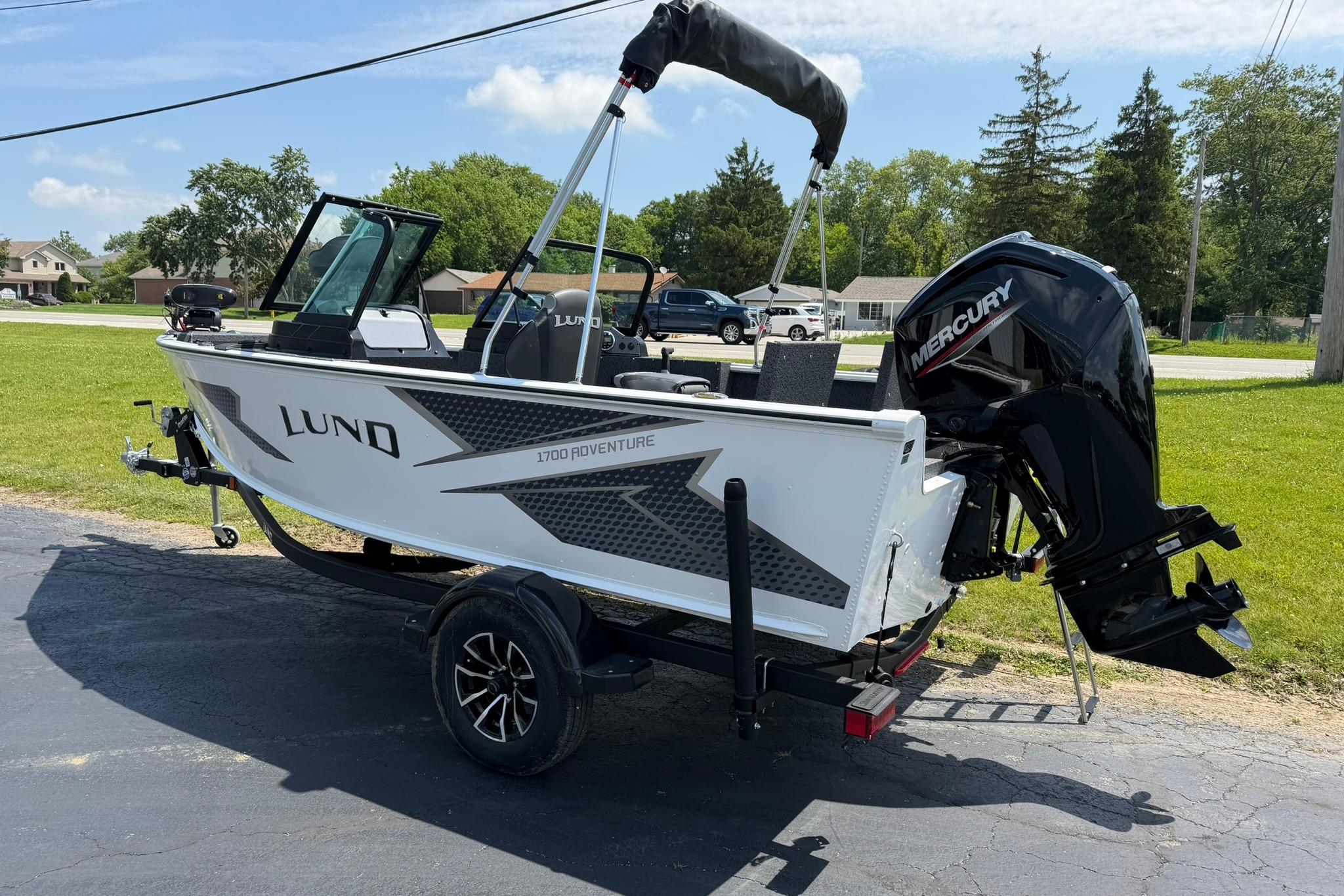 2027 Lund 1675 Adventure Sport boat with Mercury engine on trailer, parked outdoors.