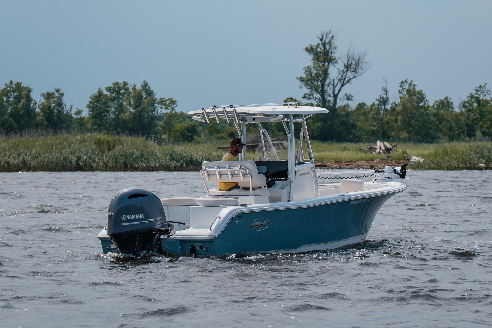2022 Sea Hunt Ultra 229 boat on water with Yamaha engine, near lush shoreline.