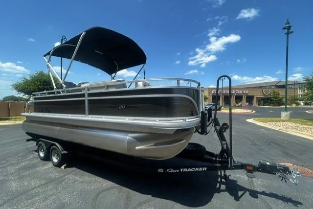 2026 Sun Tracker Fishin' Barge 20 DLX pontoon boat on trailer under clear blue sky.
