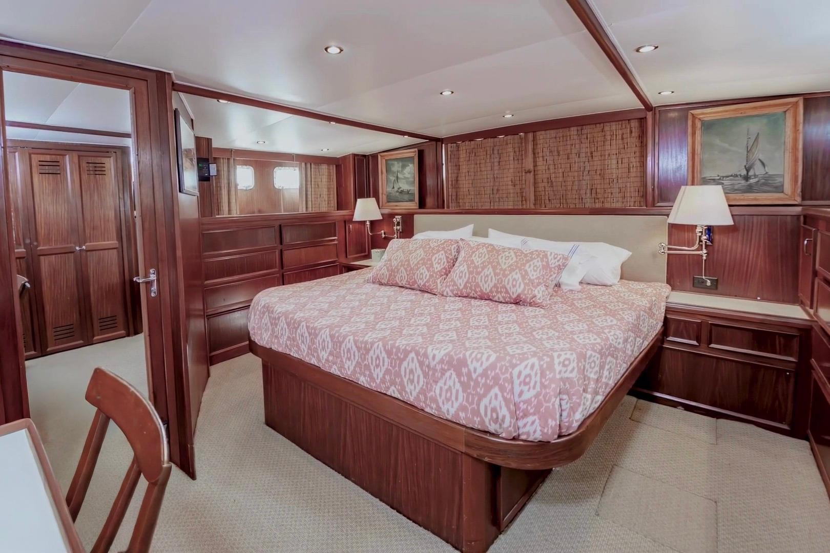 Luxurious 1980 Hatteras 70 Motor Yacht bedroom with elegant wood paneling and cozy bedding.