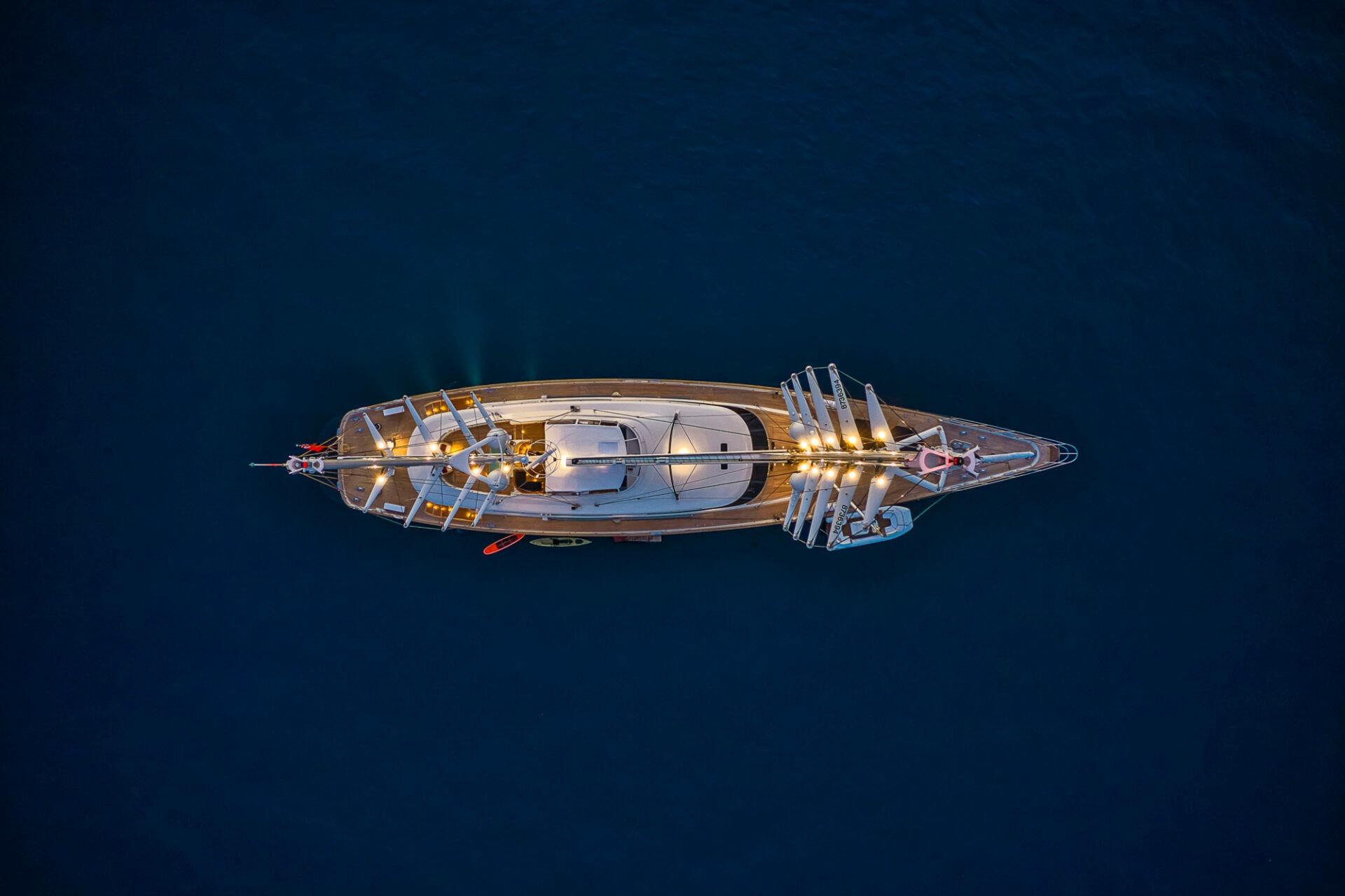 Aerial view of illuminated 2004 Perini Navi 56m yacht on dark blue water.