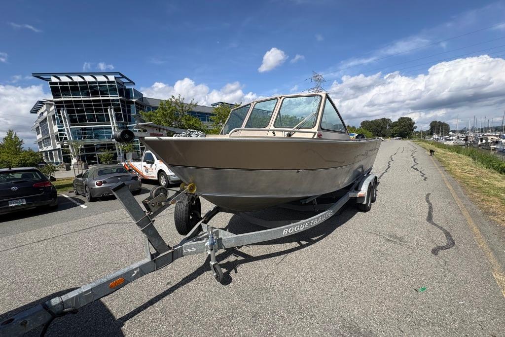 2009 Alumaweld Intruder Outboard 22 boat on trailer, parked near modern buildings and marina.