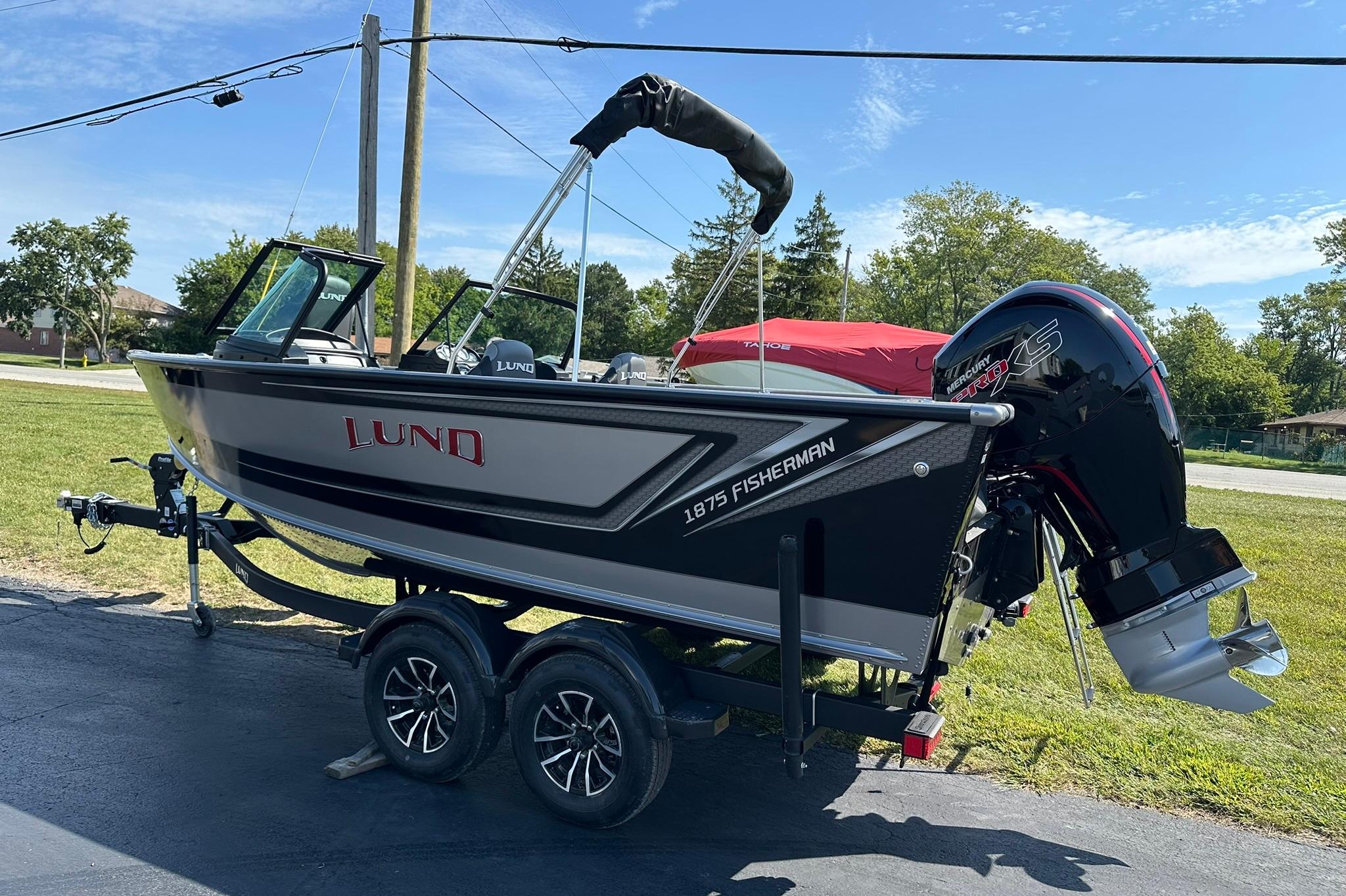 2026 Lund 1875 Fisherman boat on trailer, parked outdoors, featuring a powerful outboard motor.