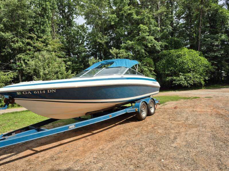 A blue and white 1996 Cobalt 220 boat on a trailer, surrounded by trees.