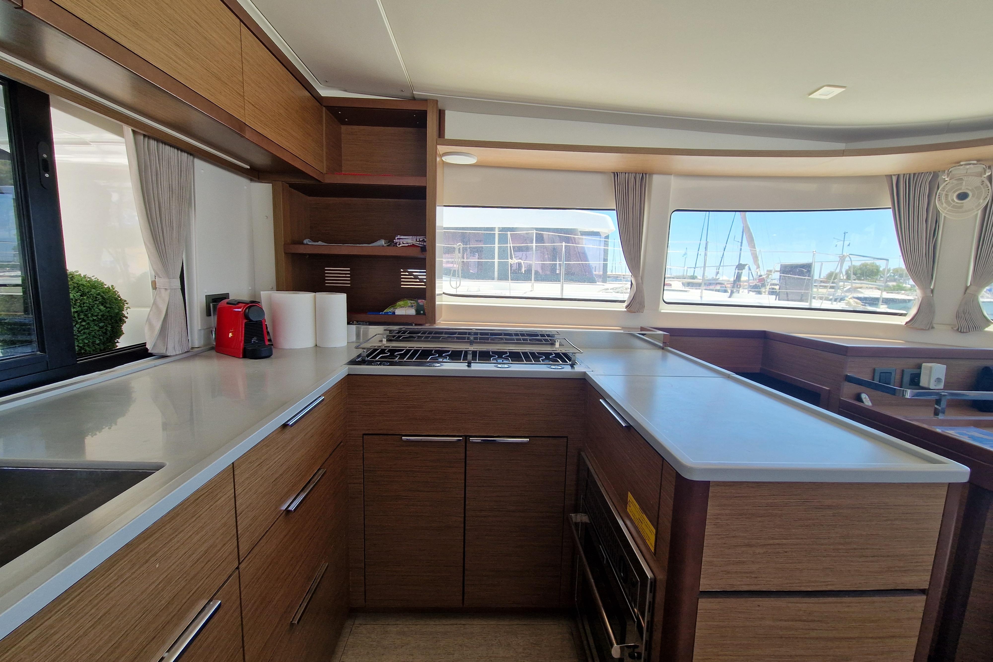 Modern kitchen interior of 2020 Lagoon 46 yacht with wooden cabinetry and large windows.