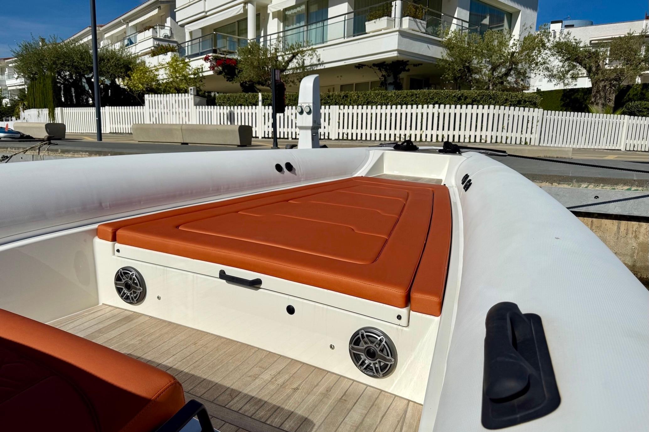 2025 Technohull 38 Grand Sport boat with orange seating, docked near modern homes.