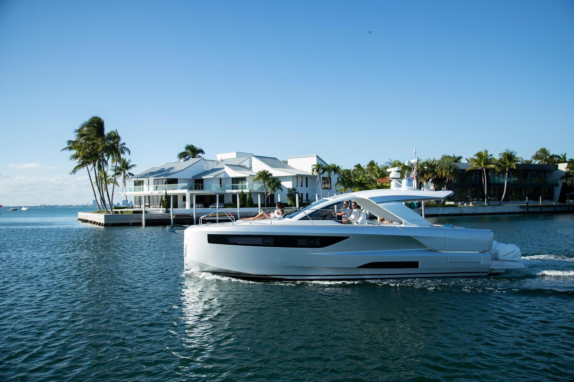 2027 Jeanneau DB/43 OB yacht cruising near waterfront homes and palm trees.