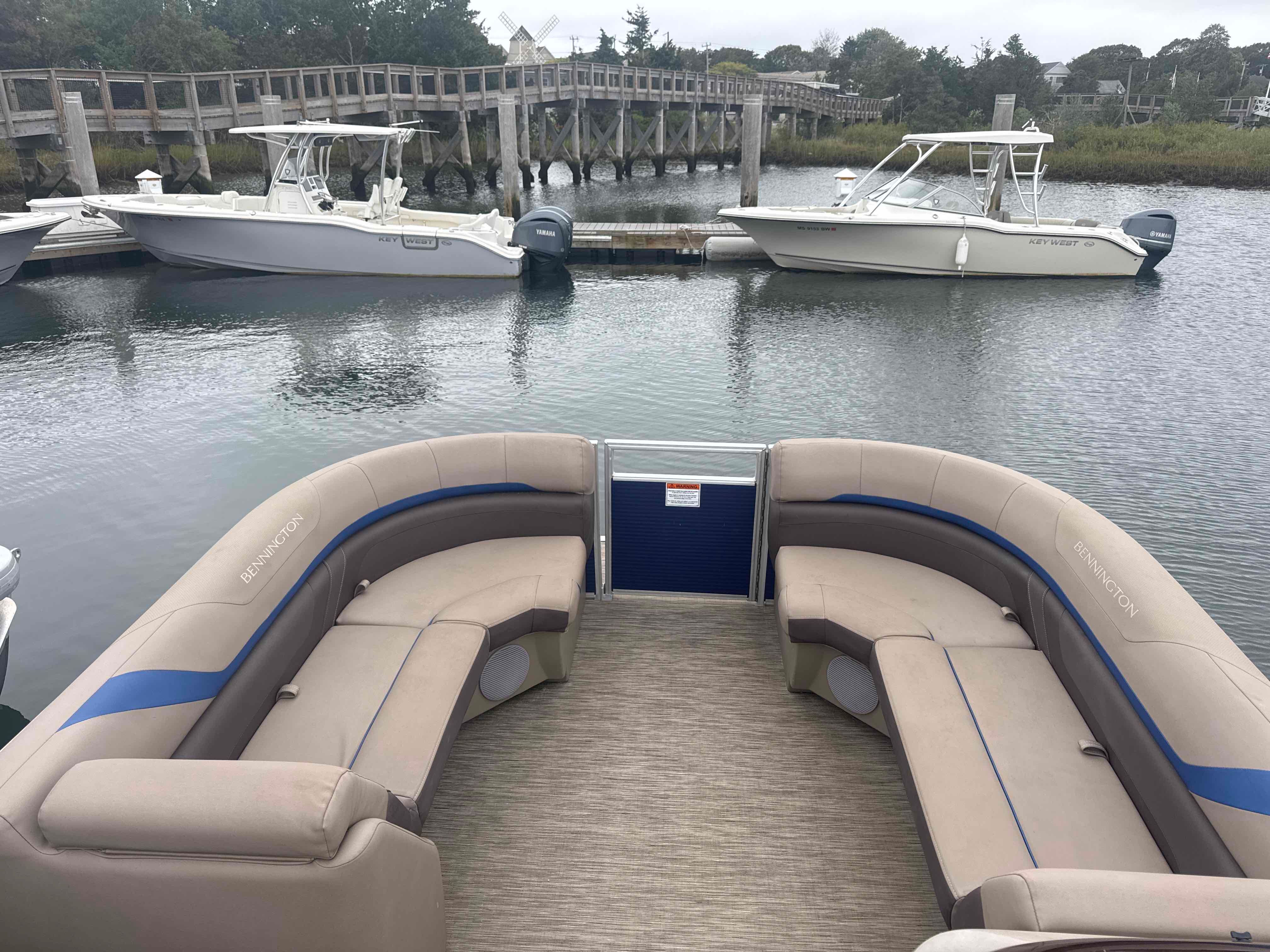 The image shows the deck of a Bennington 23SXSRC pontoon boat with beige seating and blue accents.
