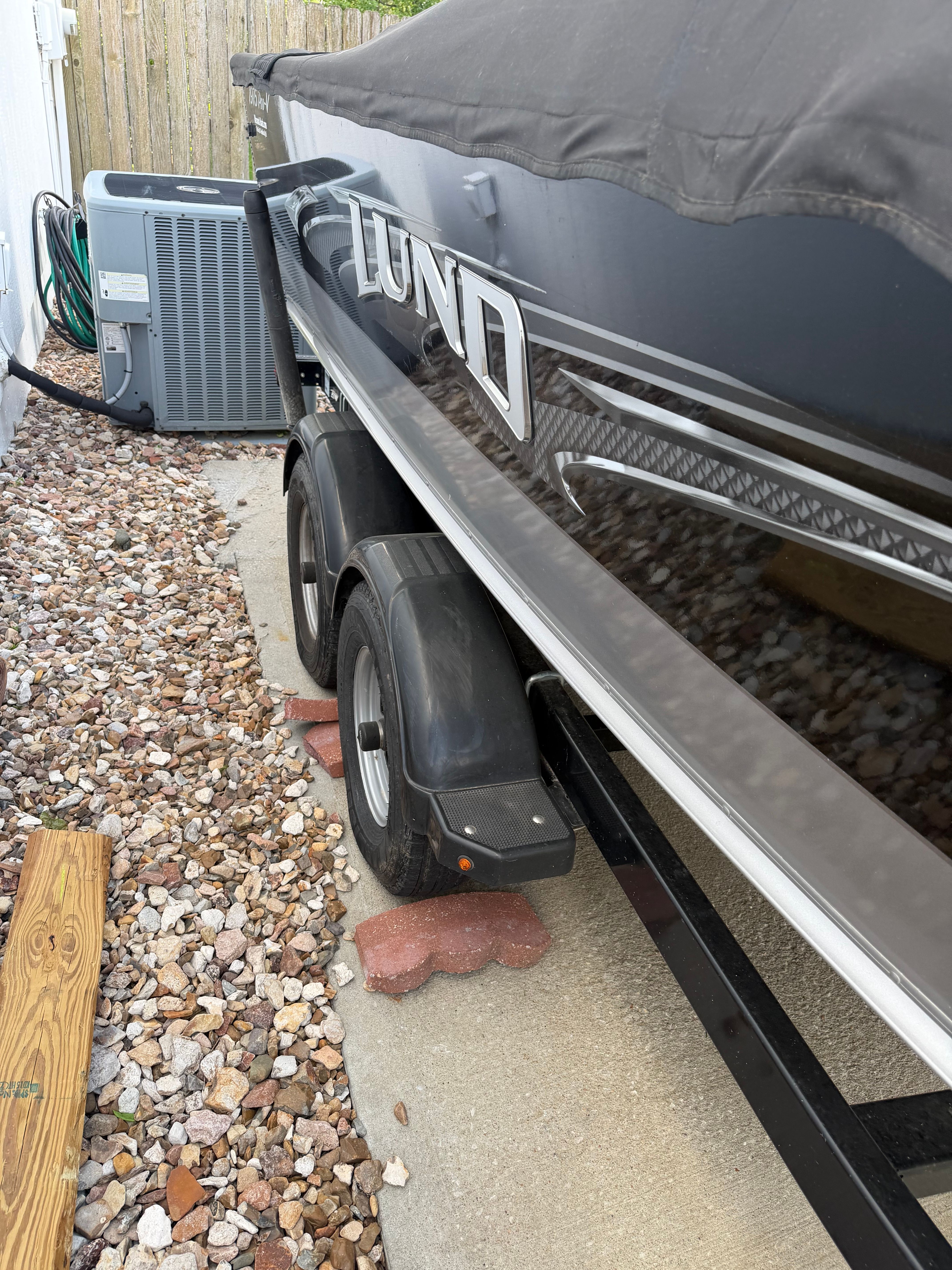 2017 Lund Pro V 1975 boat on trailer beside air conditioning unit.