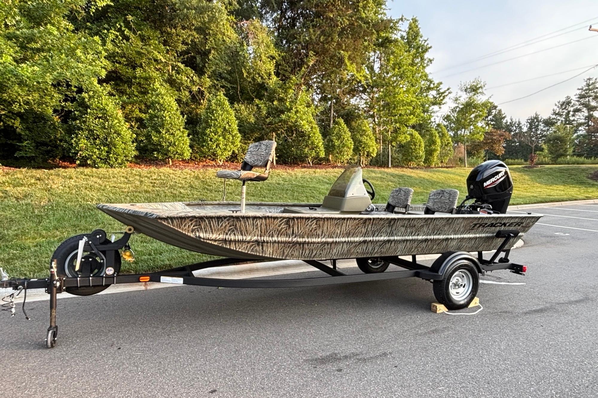 2026 Tracker Grizzly 1754 SC boat on trailer, parked outdoors with lush greenery.