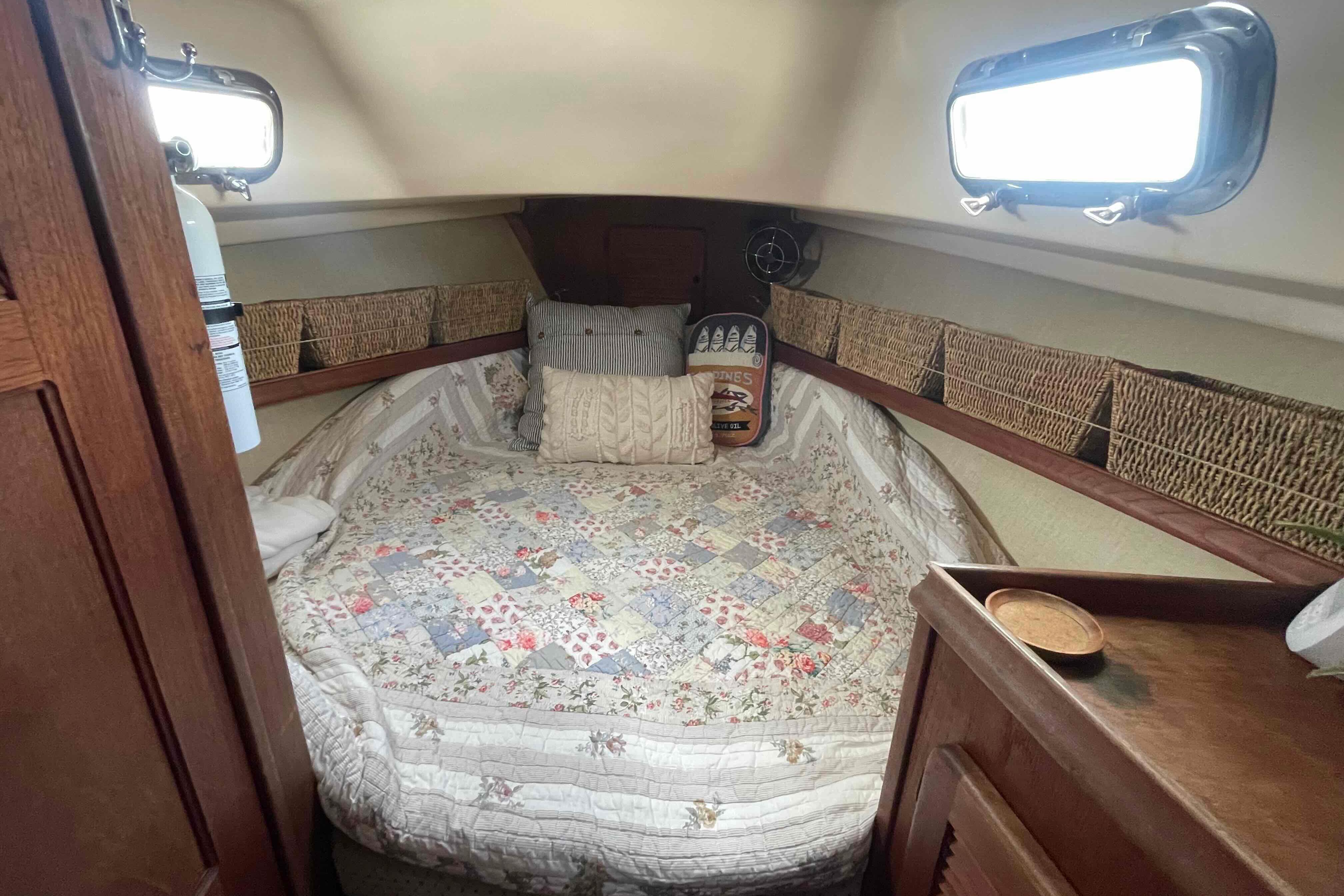 Cozy cabin interior of 1989 Island Packet 35 sailboat with quilted bedding and wicker storage.