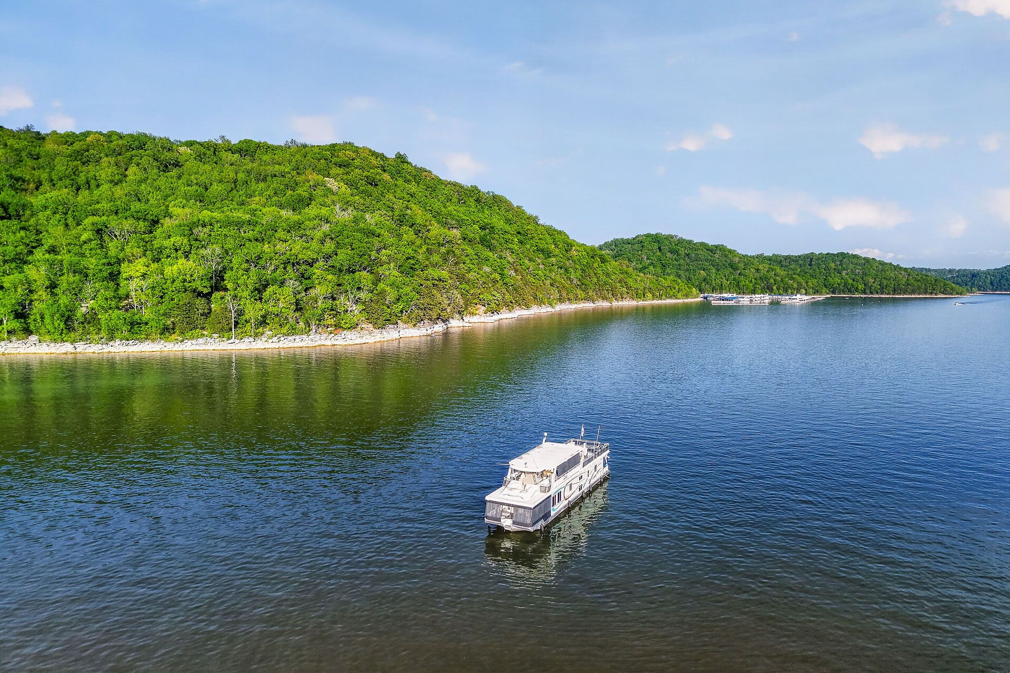Houseboat on calm lake with wooded shoreline, 2010 model.