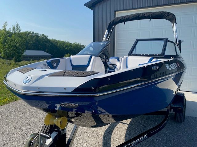 2024 Scarab 195 ID in blue, parked on a trailer in front of a garage.
