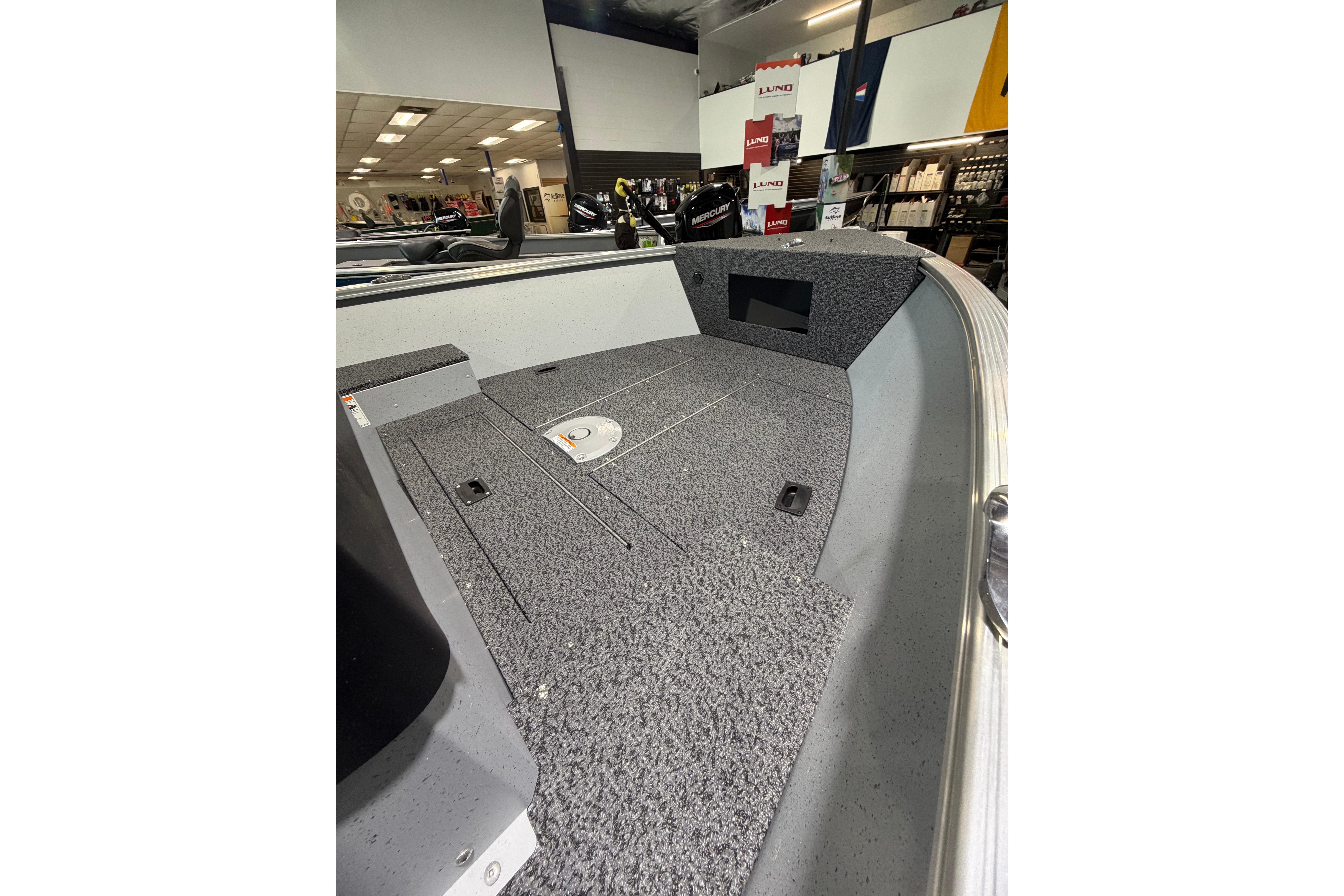 2027 Lund 1600 Fury SS boat interior with gray carpeted deck in showroom.