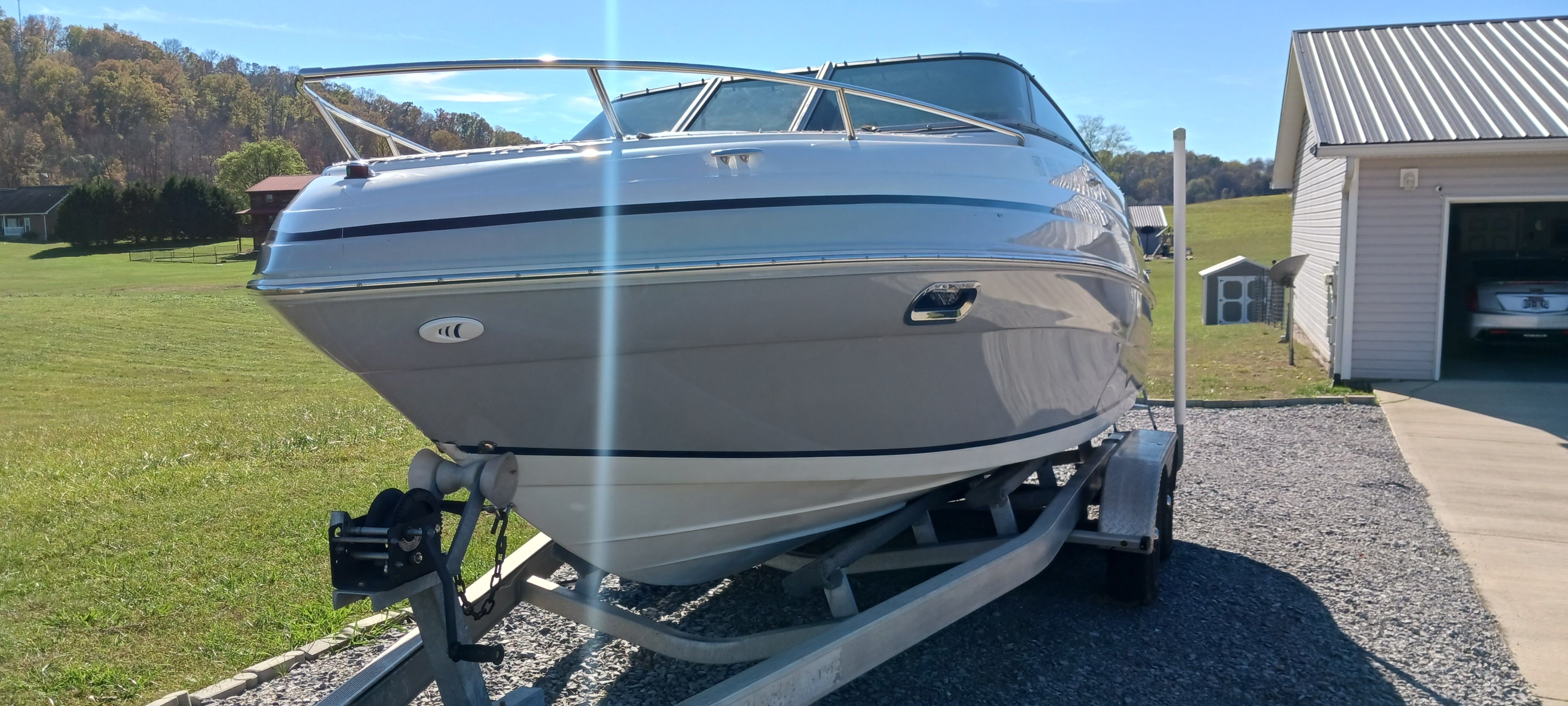 2003 Four Winns 205 Sundowner boat on trailer, parked near a garage in a rural setting.