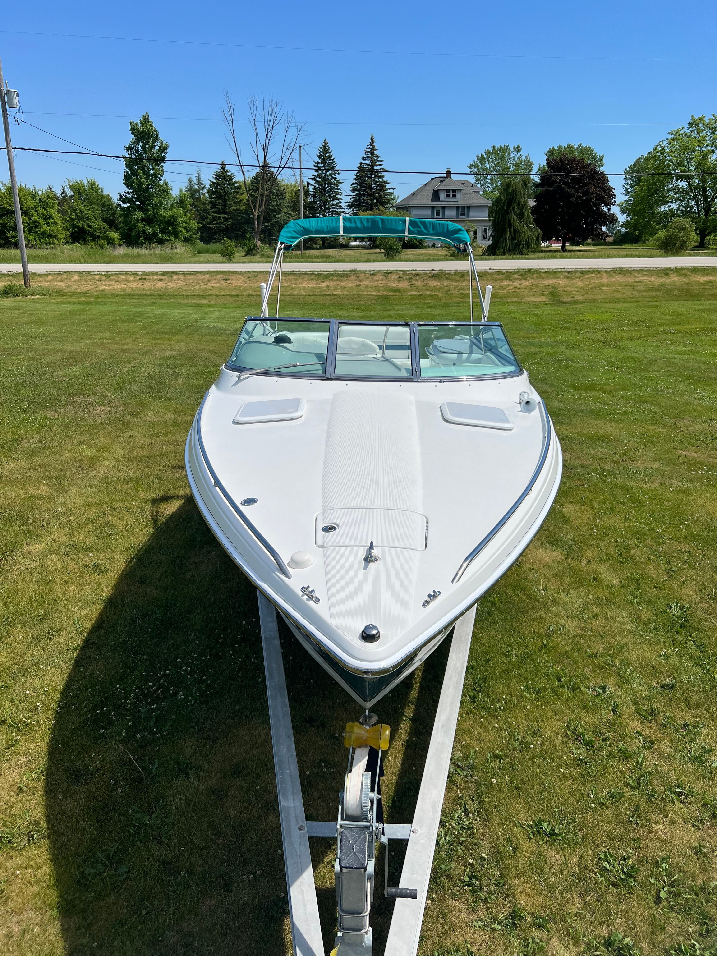 A white boat on a trailer in a grassy area, featuring a blue canopy.