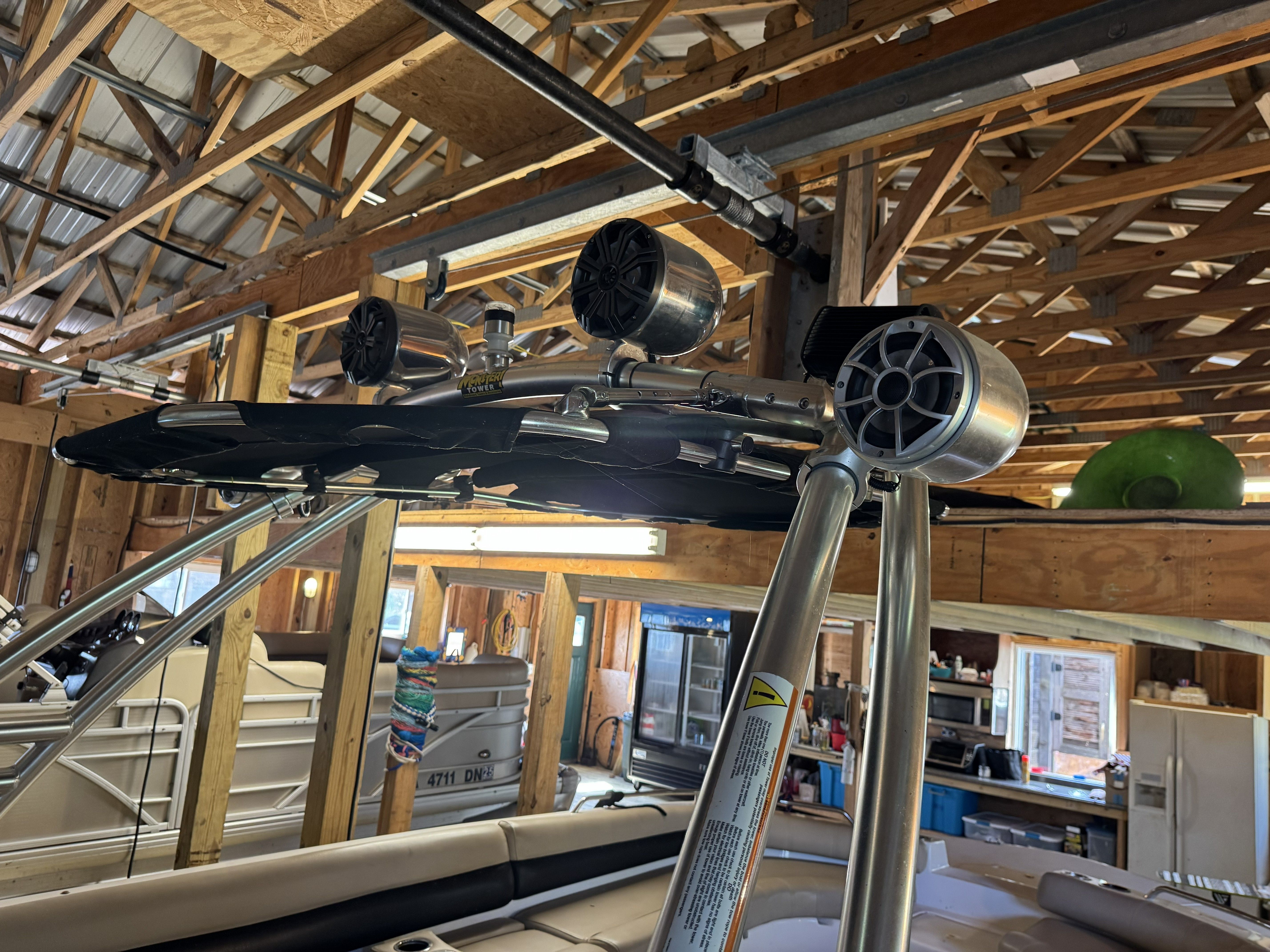 A boat with speakers and a Bimini top inside a wooden shed.