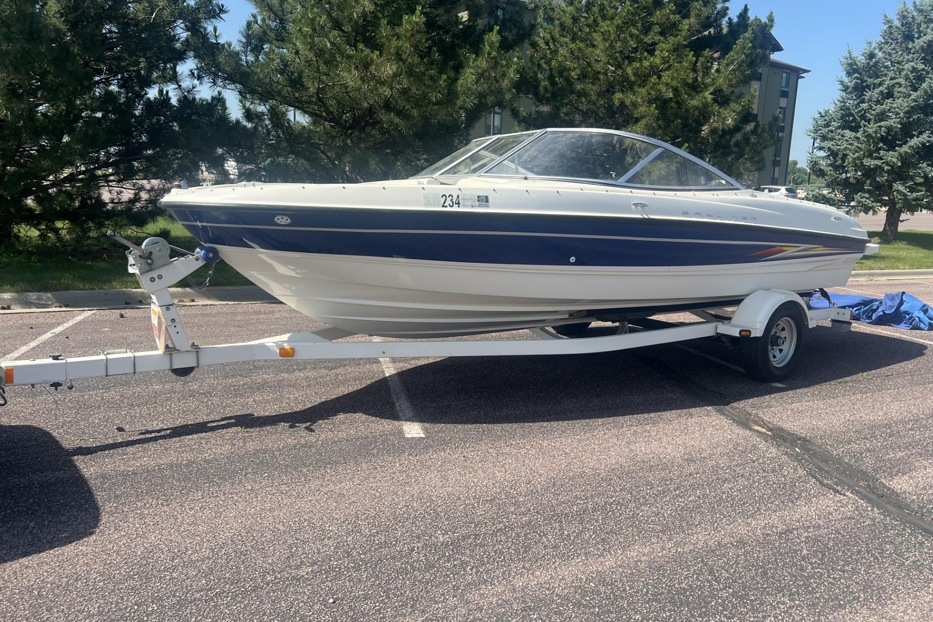 2005 Bayliner 205 Bowrider boat on trailer, parked outdoors, surrounded by trees.