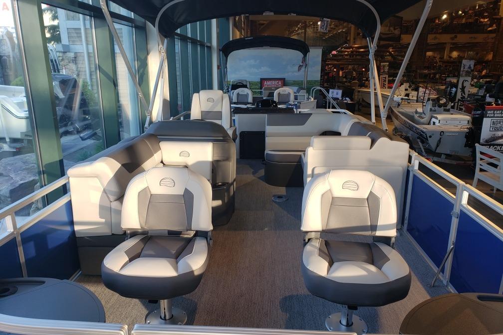 2026 Sun Tracker Fishin' Barge 20 DLX interior with seating and helm, displayed indoors.
