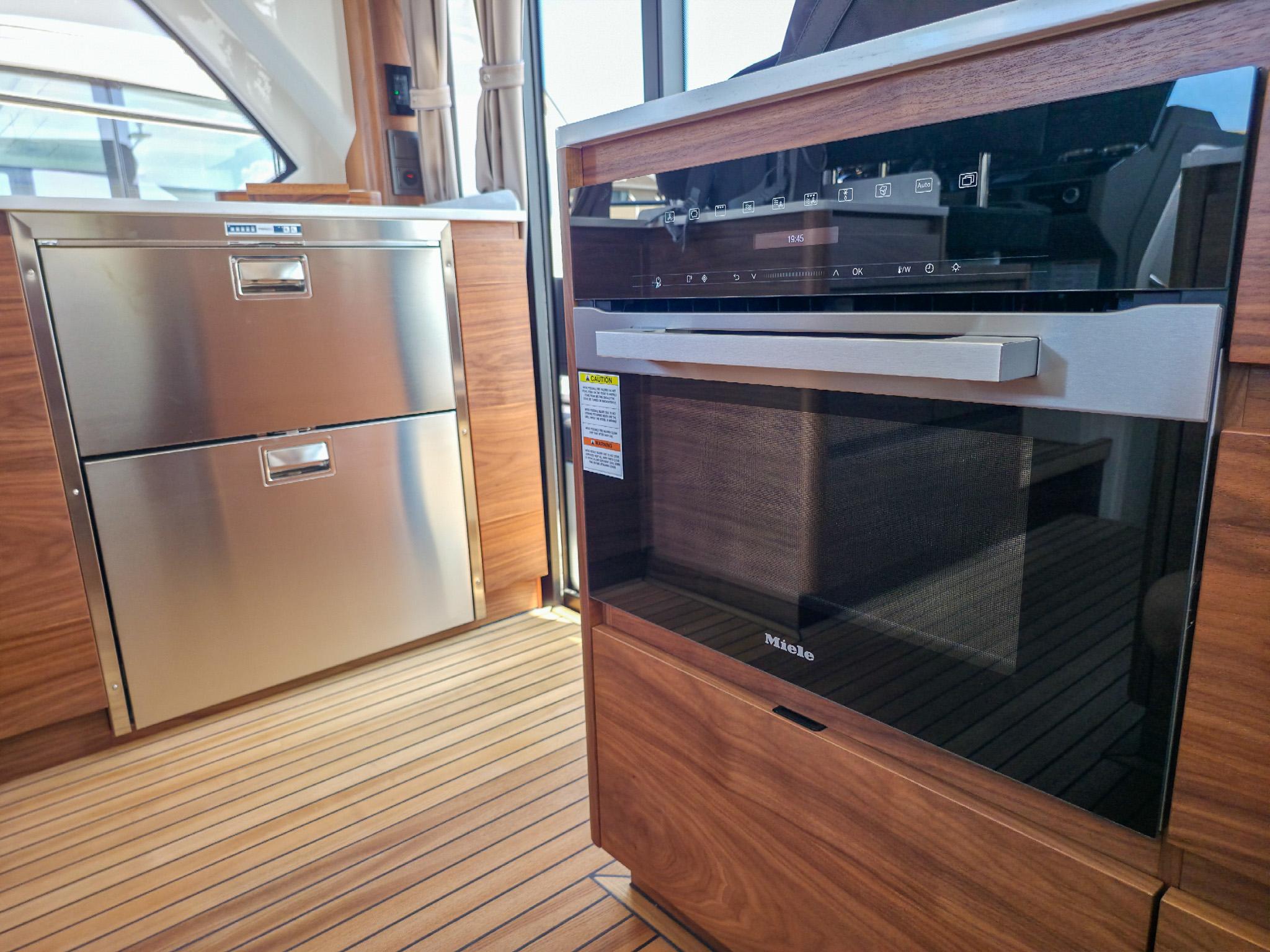 Modern kitchen interior on 2026 Marex 440 yacht, featuring Miele appliances and wood finish.
