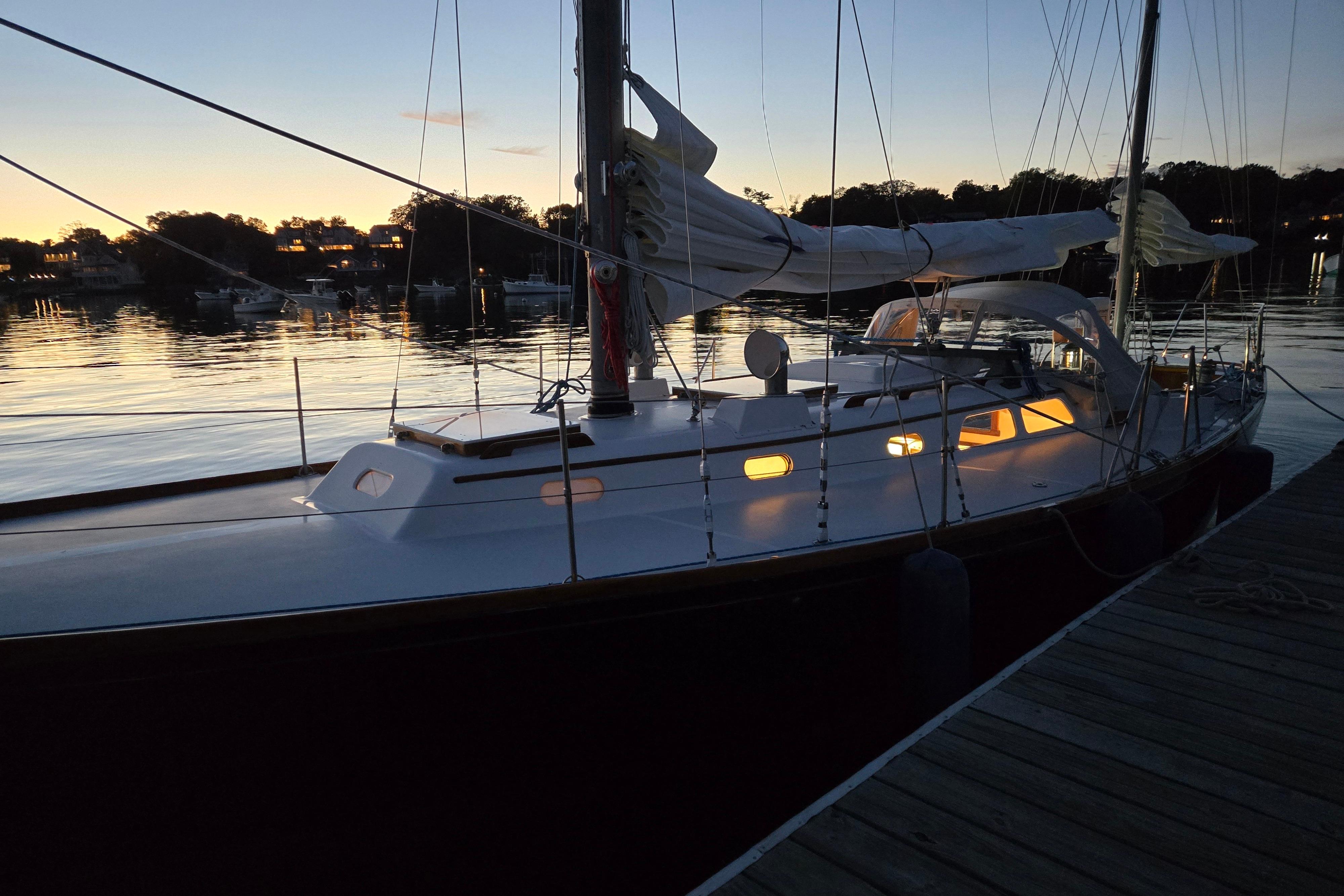 1970 Hinckley Bermuda 40 sailboat docked at sunset, with illuminated cabin windows.