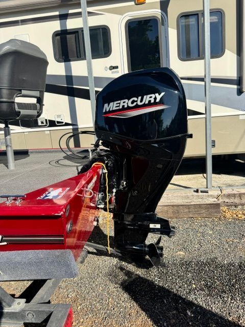 A Mercury outboard motor is attached to a red boat on a trailer.