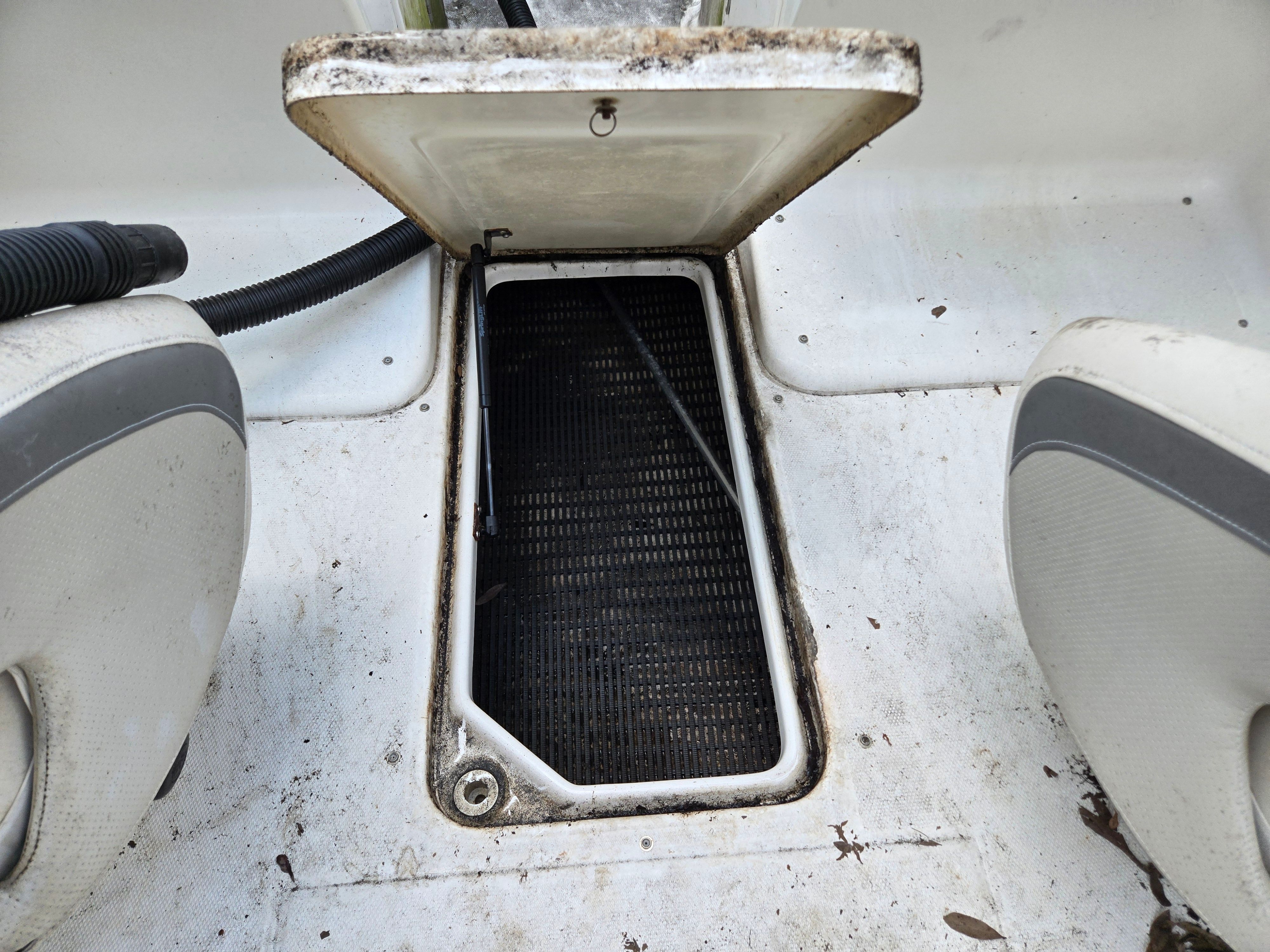 An open storage compartment on a boat with two seats beside it.