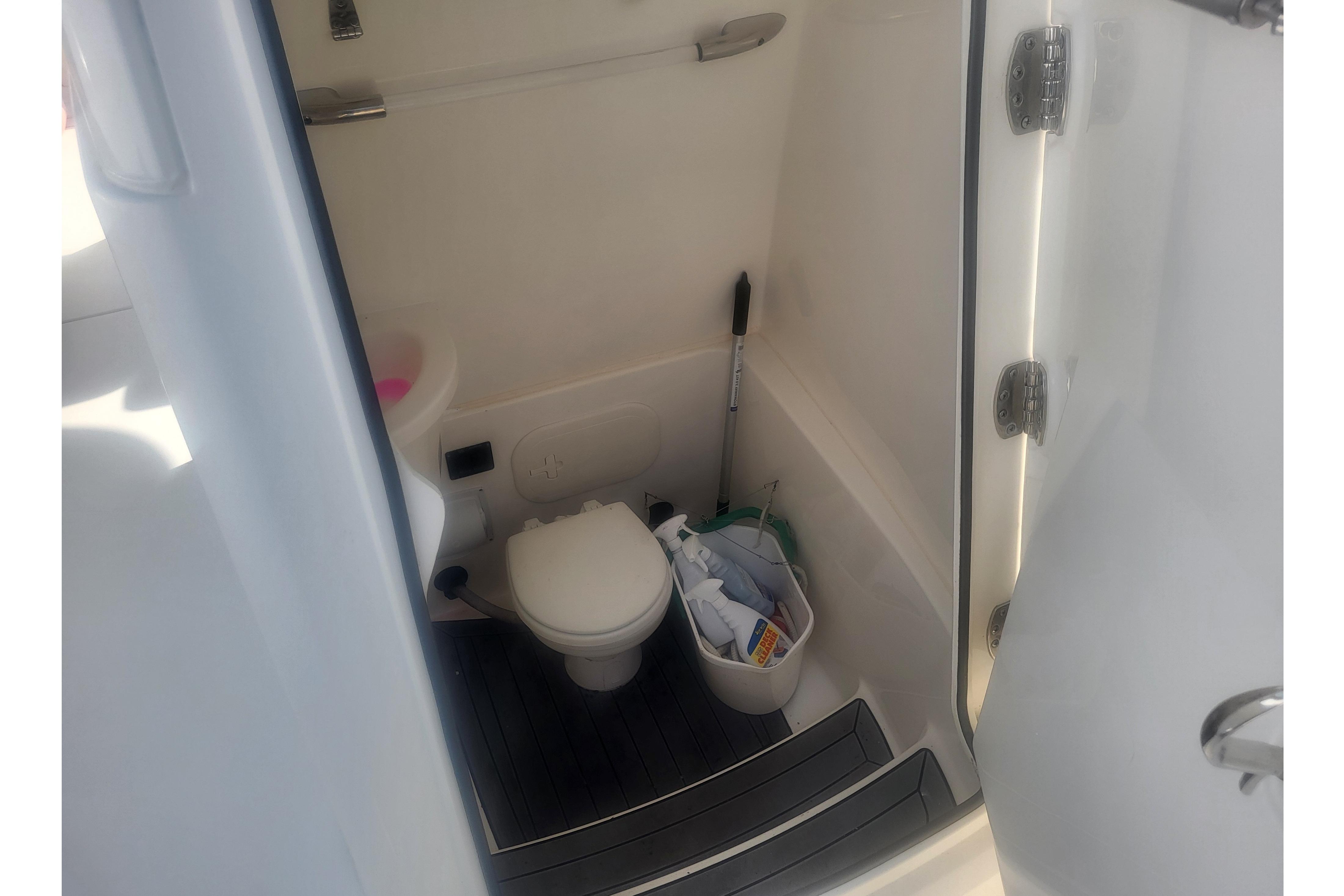 Interior of 2022 Cobia 262 Center Console boat's compact bathroom with toilet and cleaning supplies.