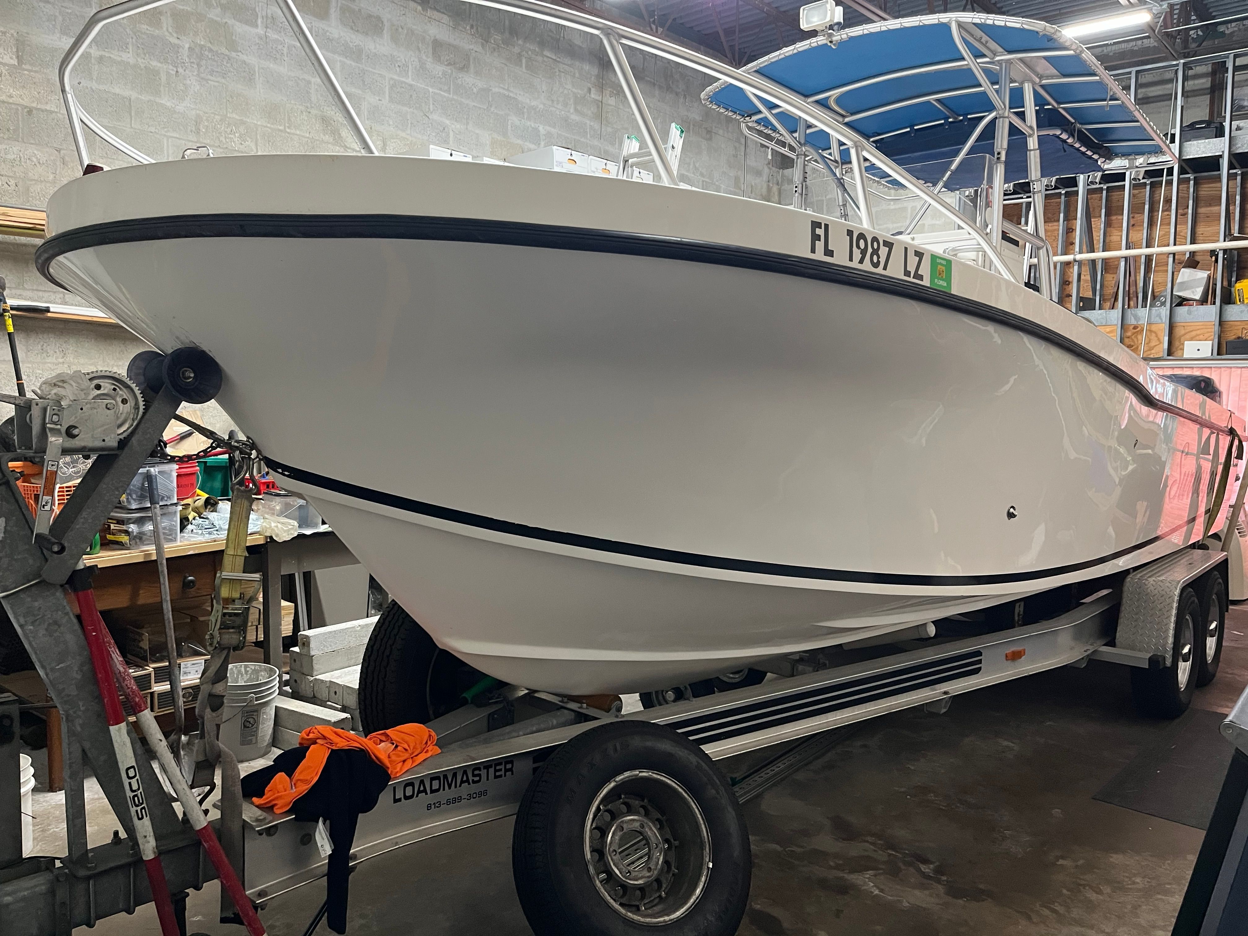 A white 2002 Dusky 25.6 boat on a trailer in a garage setting.