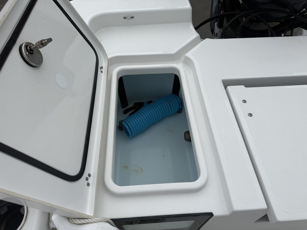 An open storage compartment on a Sportsman Masters 247OE Bay Boat with a blue hose inside.