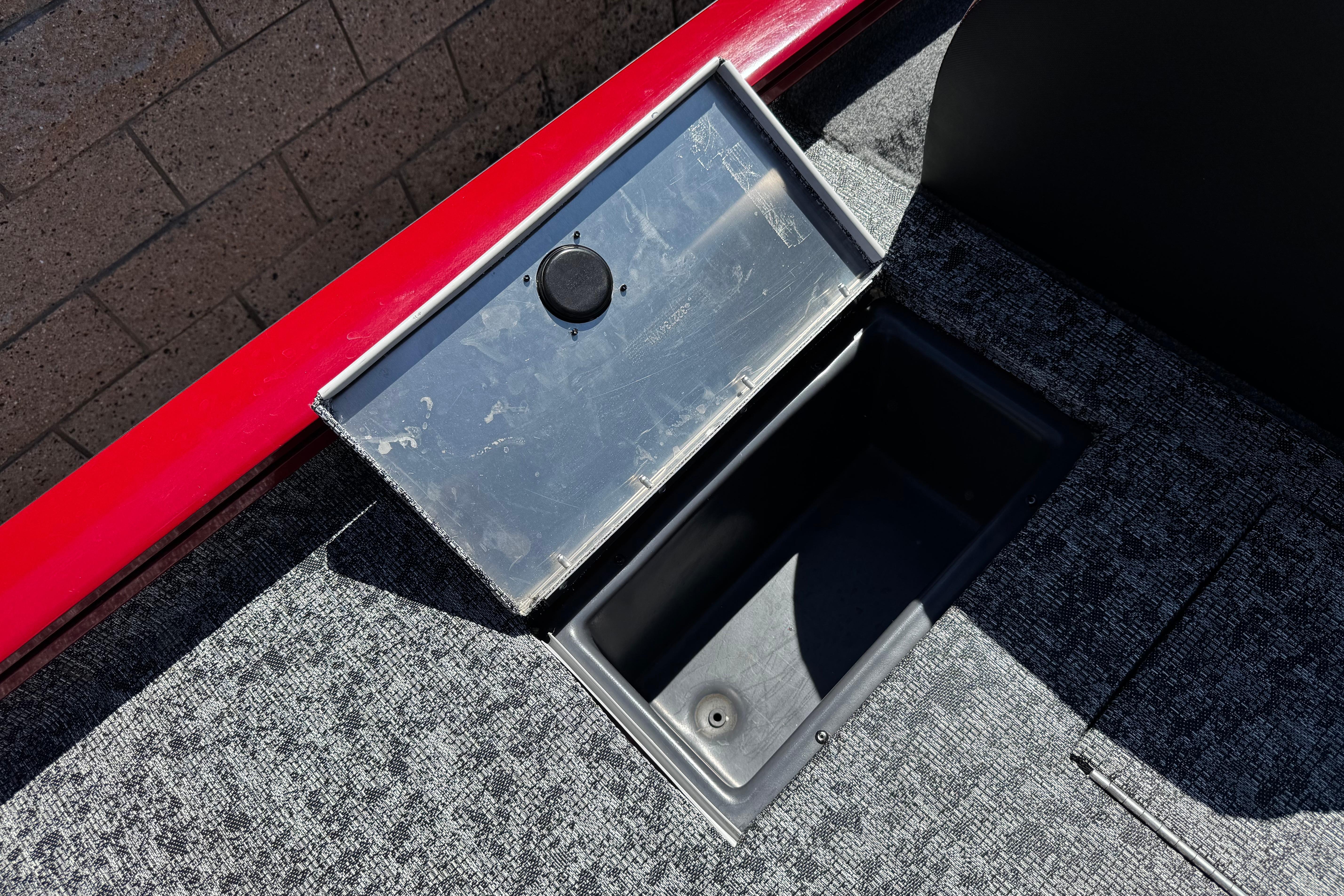 Open storage compartment on 2025 Tracker Pro Team 175 TXW boat, featuring red trim and gray carpet.