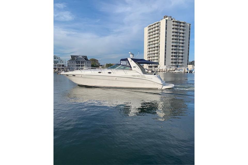 1999 Sea Ray Sundancer 400 yacht cruising near waterfront buildings under a clear sky.